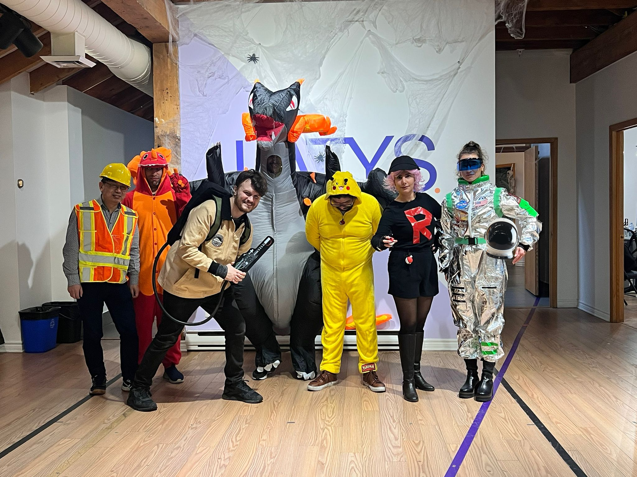 Group of people in Halloween costumes posing for a photo indoors, with Halloween-themed decorations in the background.