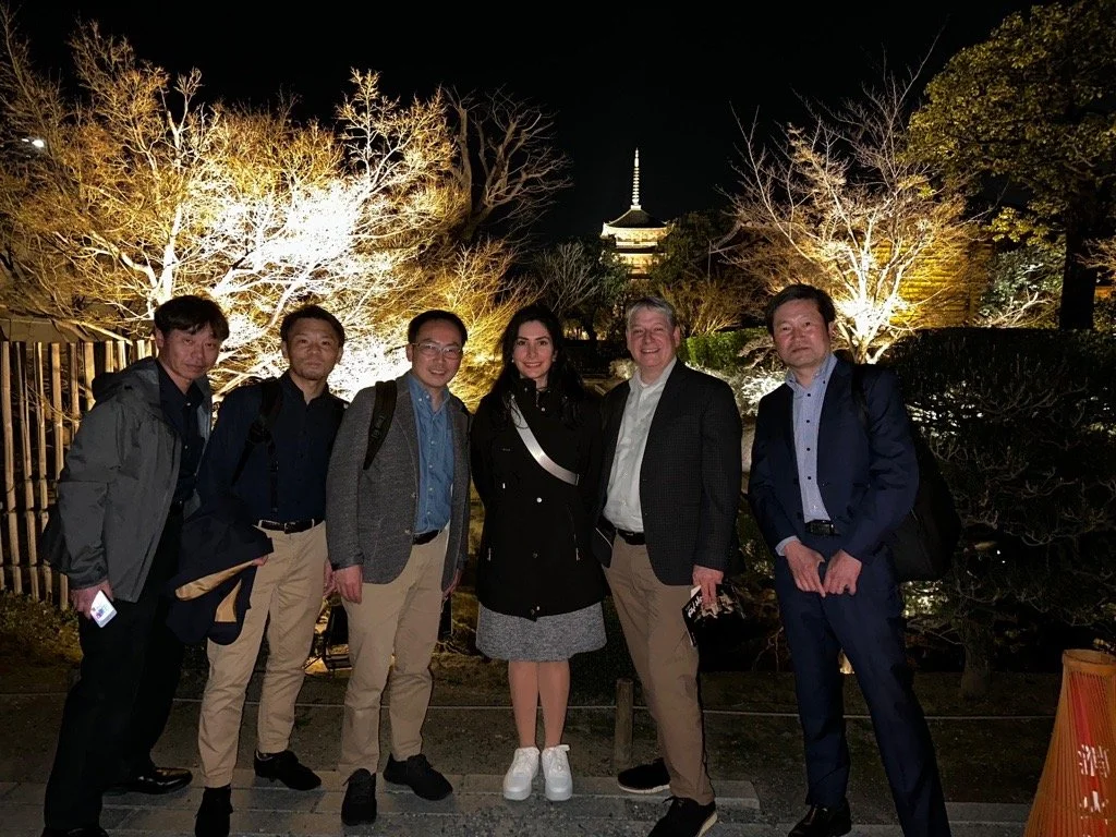 Group of six people standing together at night, illuminated trees and a pagoda-like structure in the background.