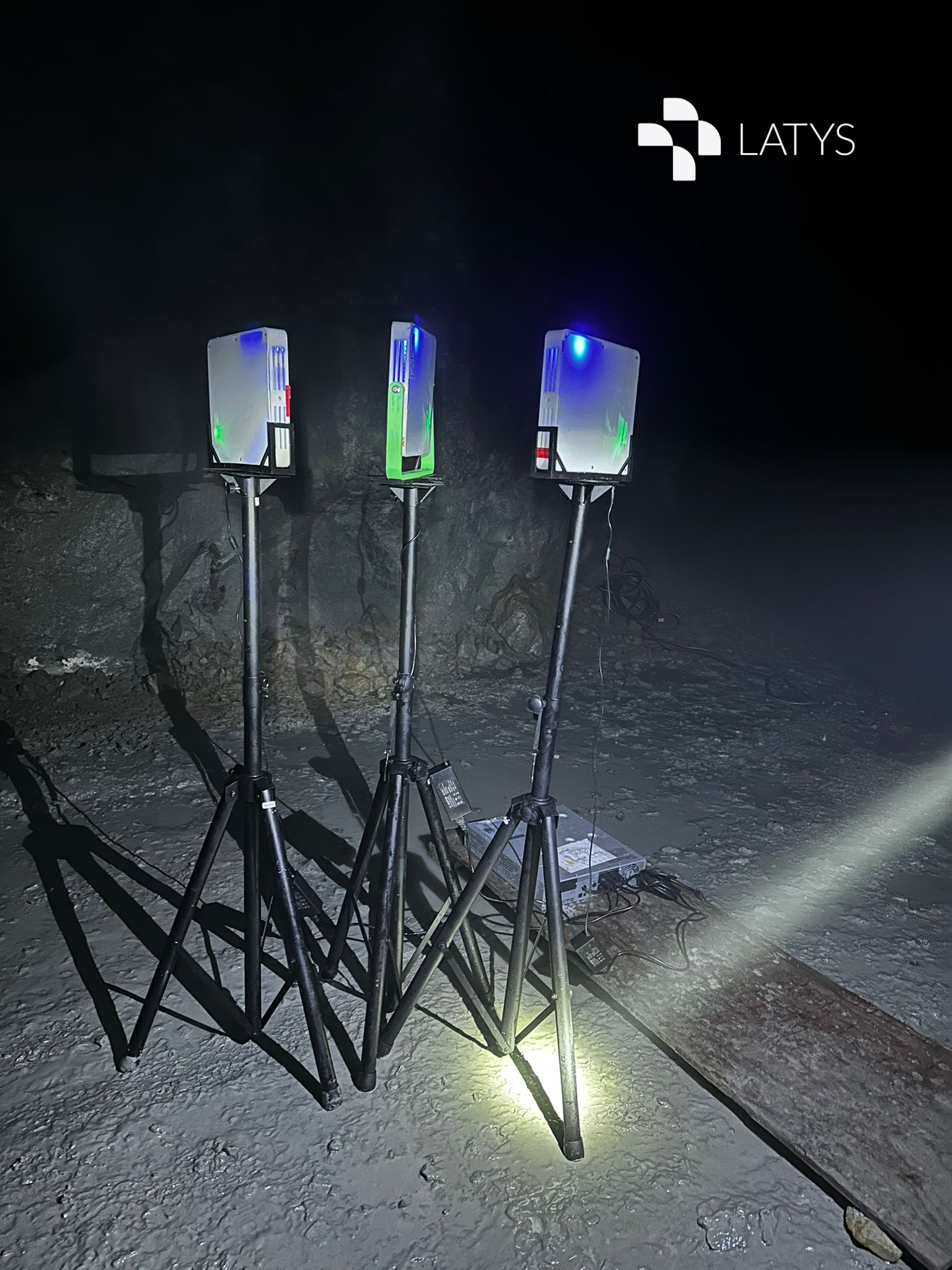 Three scientific or industrial equipment units with illuminated indicators, set up on a snowy or icy surface in a dark environment, with cables and a control box nearby.