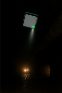 A sewer pipe with a mounted inspection camera emitting a light, and water reflecting the light in a dark environment.