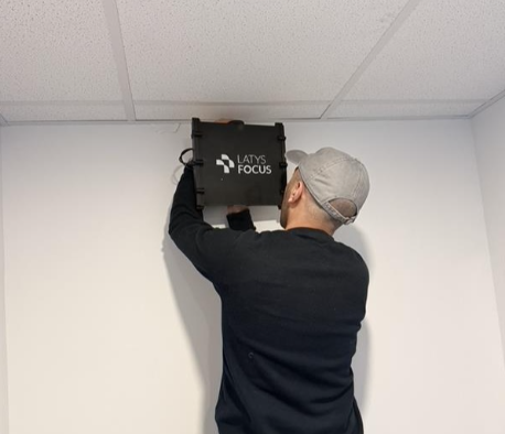 A man installing or working with a projector or electronic device on a ceiling, with