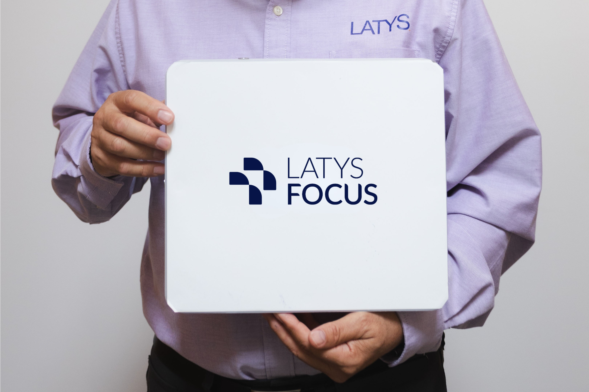 Person in a lavender shirt holding a white box with the logos LATYS and FOCUS printed on it.