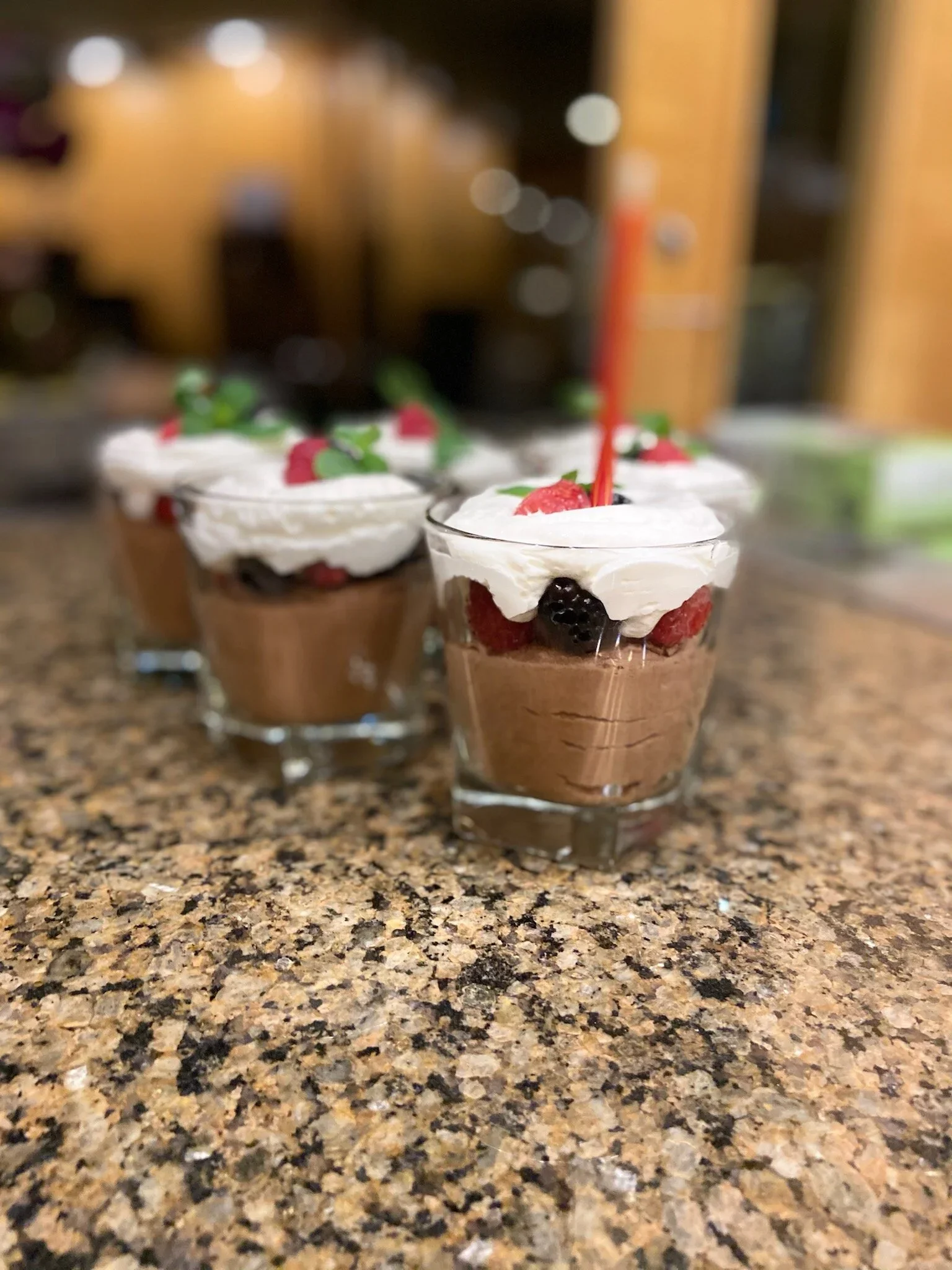 Dessert glasses with rich chocolate mousse, Chantilly whipped cream, fresh berries, and a red birthday candle on top for a luxury plated birthday dinner party.