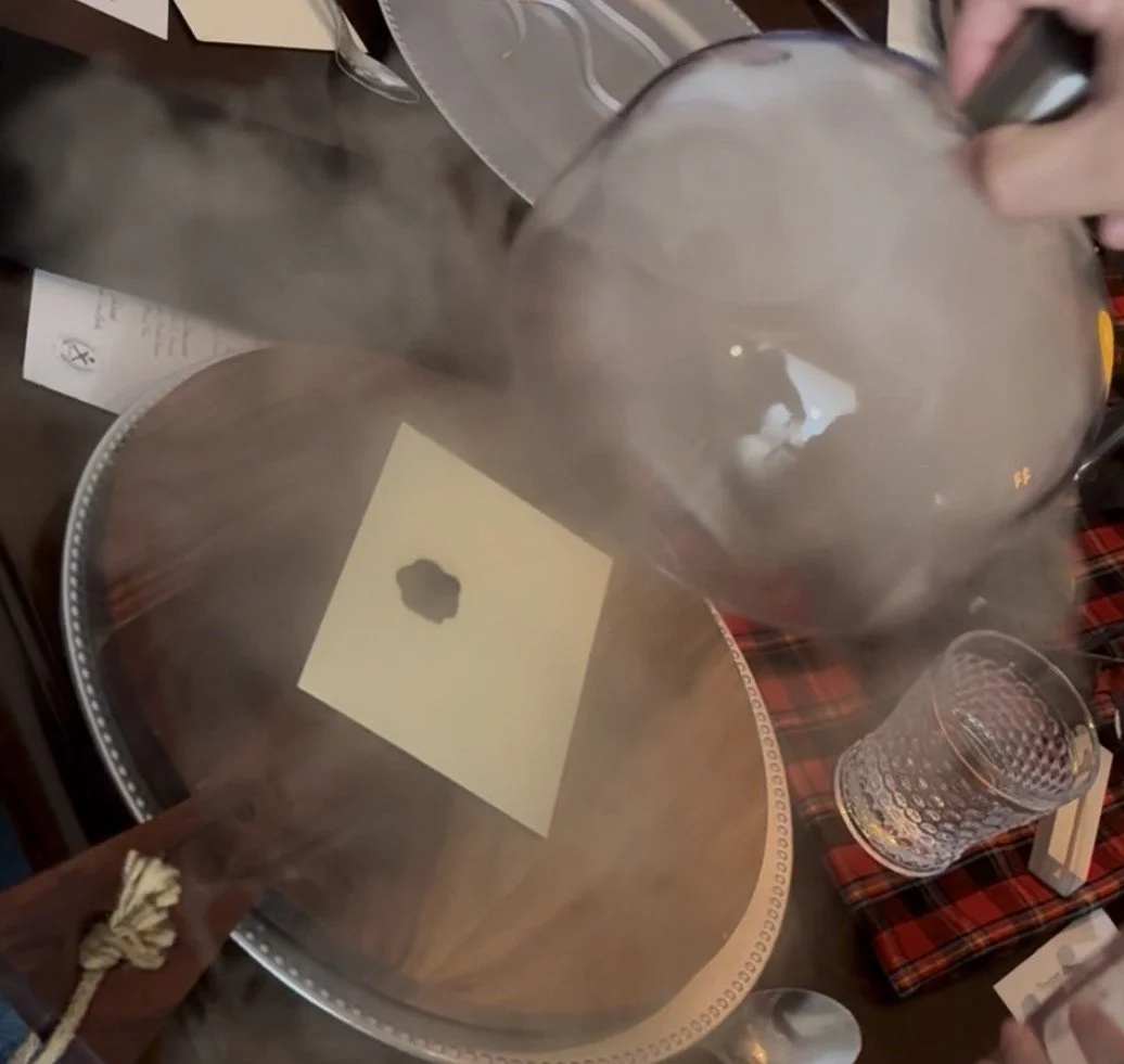 Smoke billows from a lifted glass dome, revealing a black‑wax‑sealed envelope resting on a wooden tray in a dramatic final‑reveal moment.