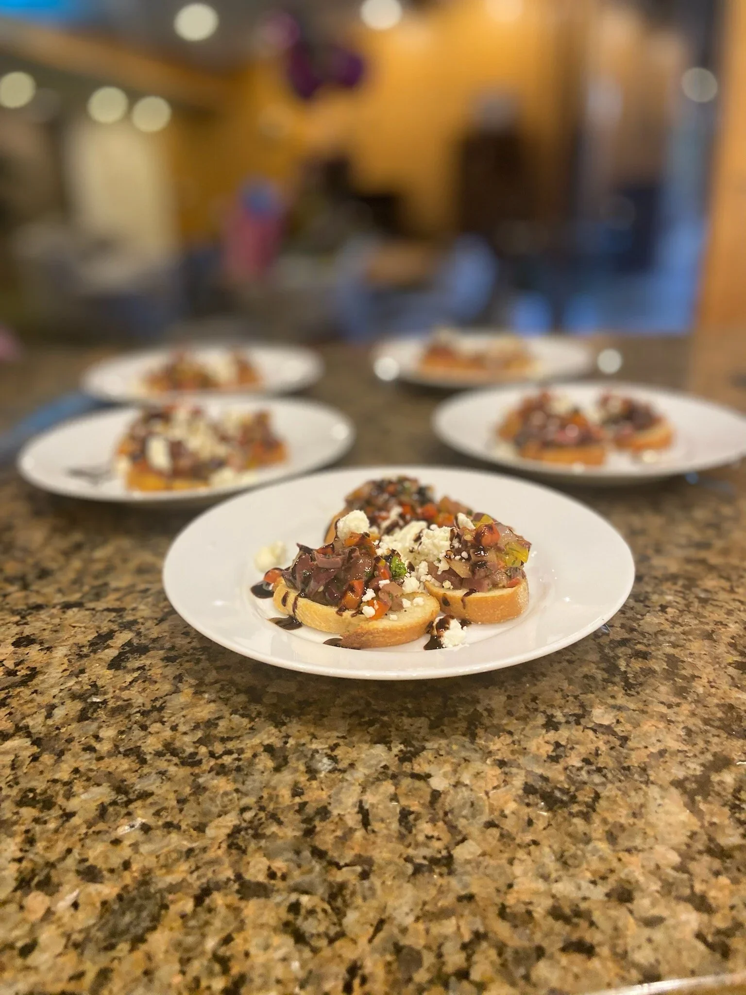 Close-up of a plate with an Athenian appetizer, a crostini topped with a blend of olives, red onion, feta cheese and balsamic glazeon a granite countertop in a Luxury kitchen in Scottsdale, Az.