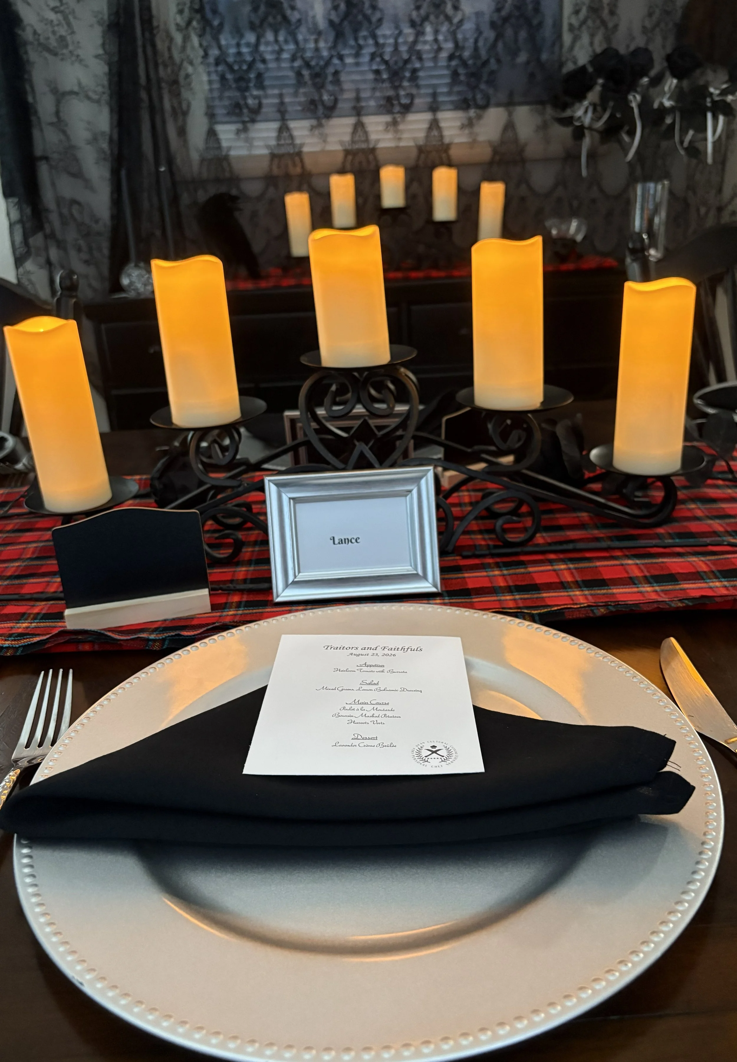 Close‑up of a silver dinner plate on a tartan table runner with dramatic low lighting creating a moody, immersive dining atmosphere.