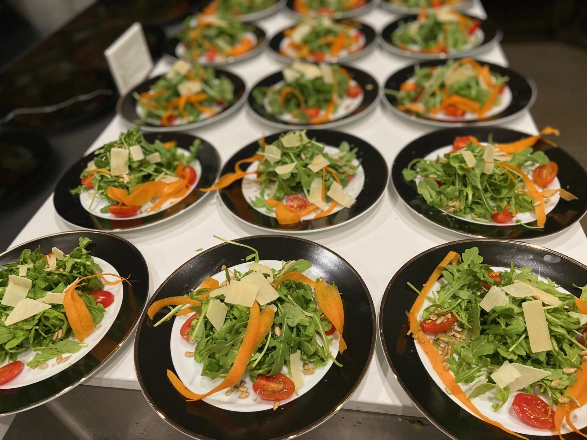 Multiple plates of fresh salad with arugula, cherry tomatoes, shredded carrots, cheese shavings, and sunflower seeds on a white table for a luxury dinner party in Cave Creek, Az.