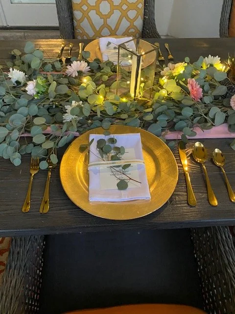 Luxury table setting with gold charger plates, gold flatware, and an illuminated eucalyptus runner centerpiece for a private chef dinner experience.