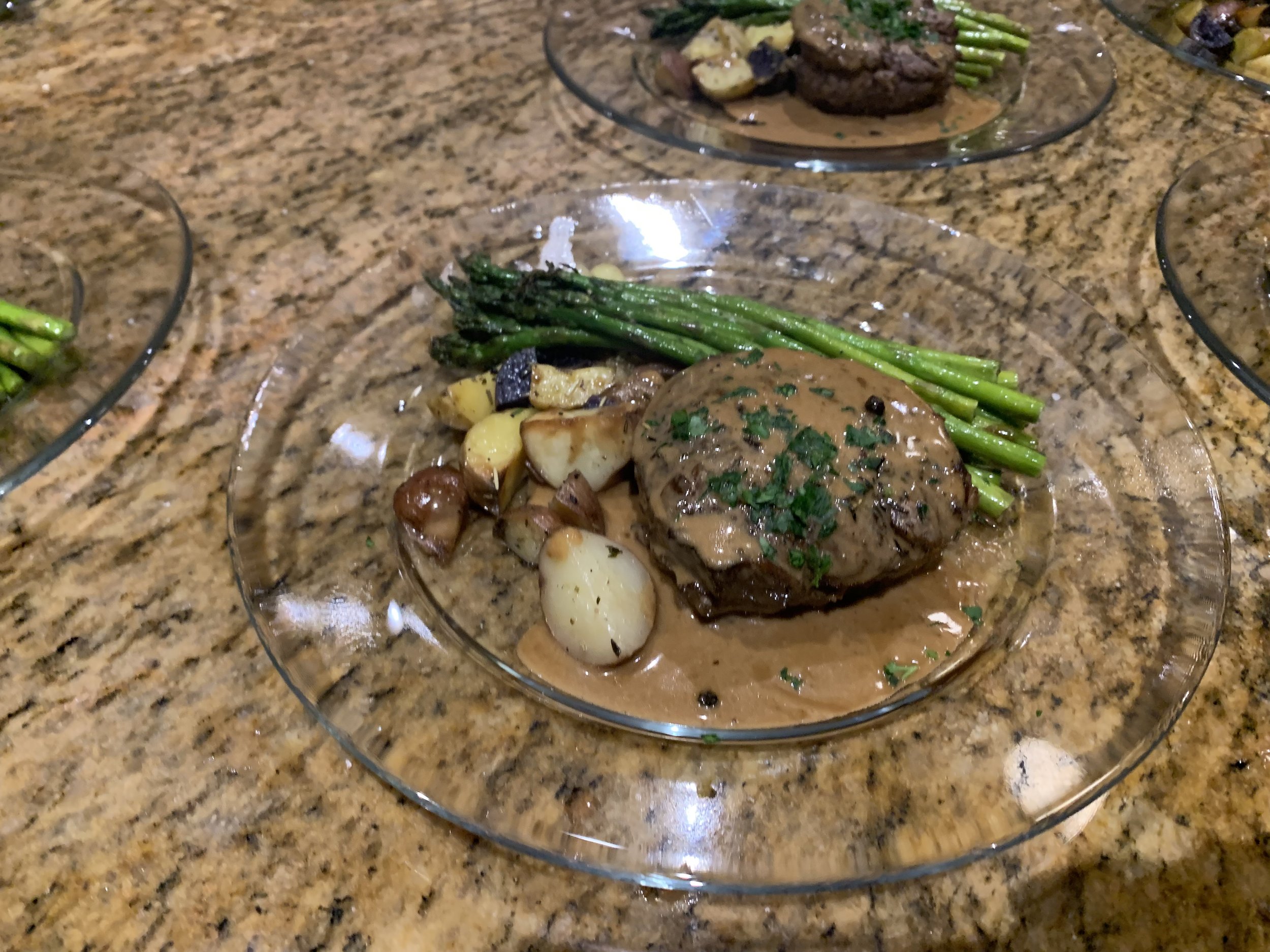 Filet mignon steak entrée with rich peppercorn cream sauce, fresh asparagus spears, and roasted fingerling potatoes plated on clear glass plates for a luxury private dinner in Paradise Valley.