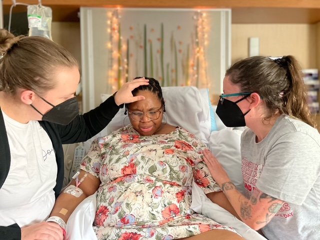 A person in a floral labor gown supported by two doulas