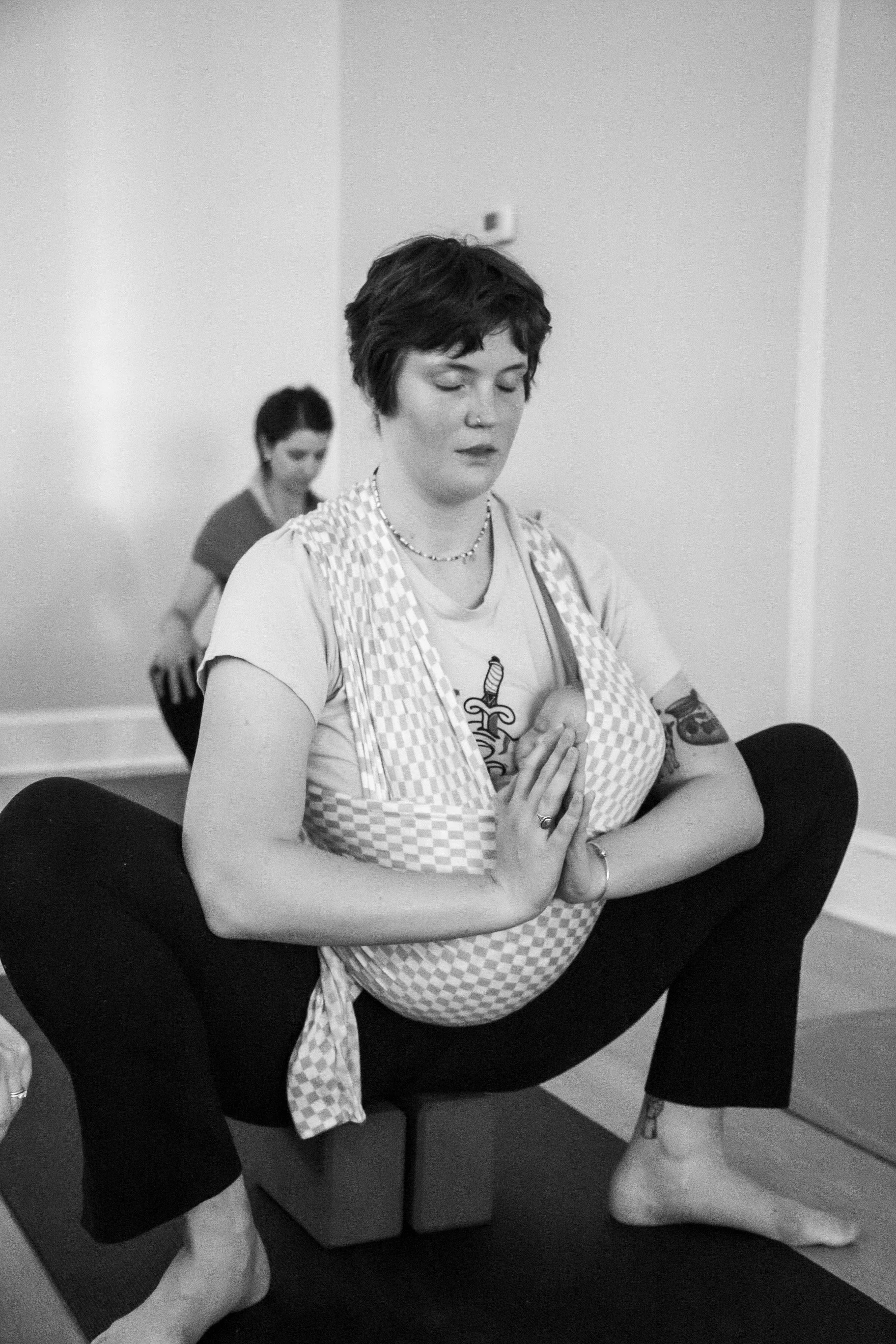 A black and white photo of Tend doula Colleen in a yoga squat while wearing a baby in a stretchy carrier