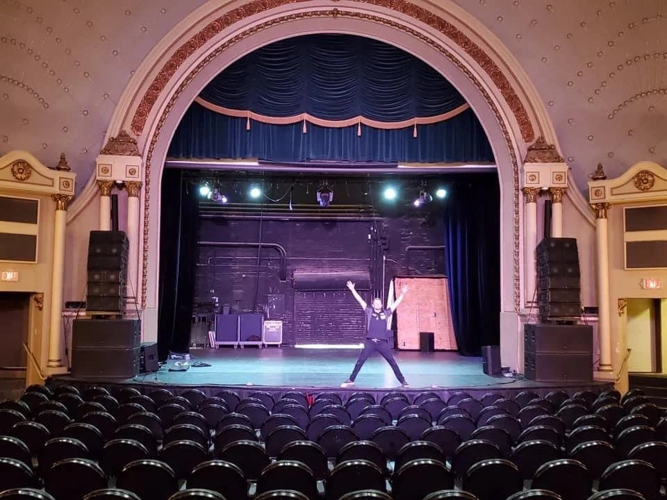 Performer practicing dance on stage in an empty theater with rows of seats