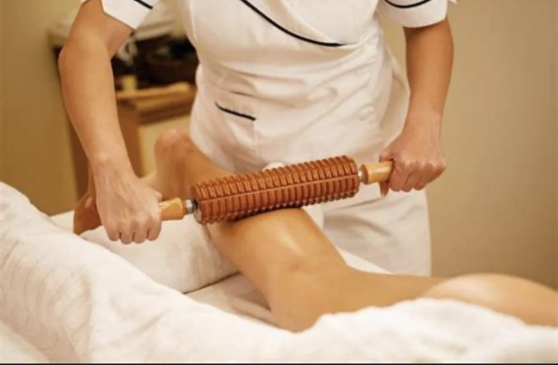 Person receiving a hot stone massage on their thigh with a massage roller in a spa or massage room.