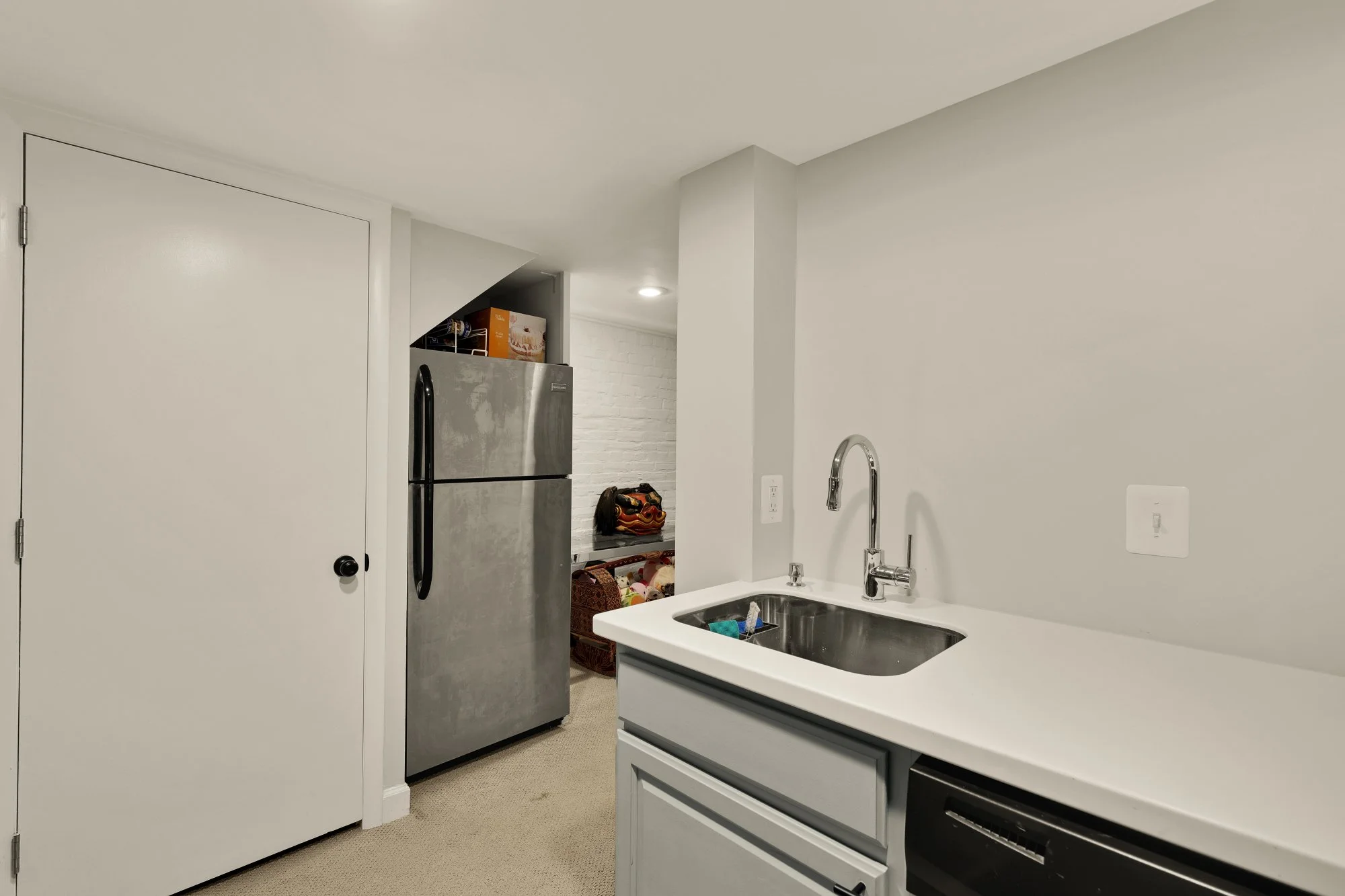 A modern kitchen with white walls, a stainless steel refrigerator, a white cabinet with black trim, and a stainless steel sink with a chrome faucet.