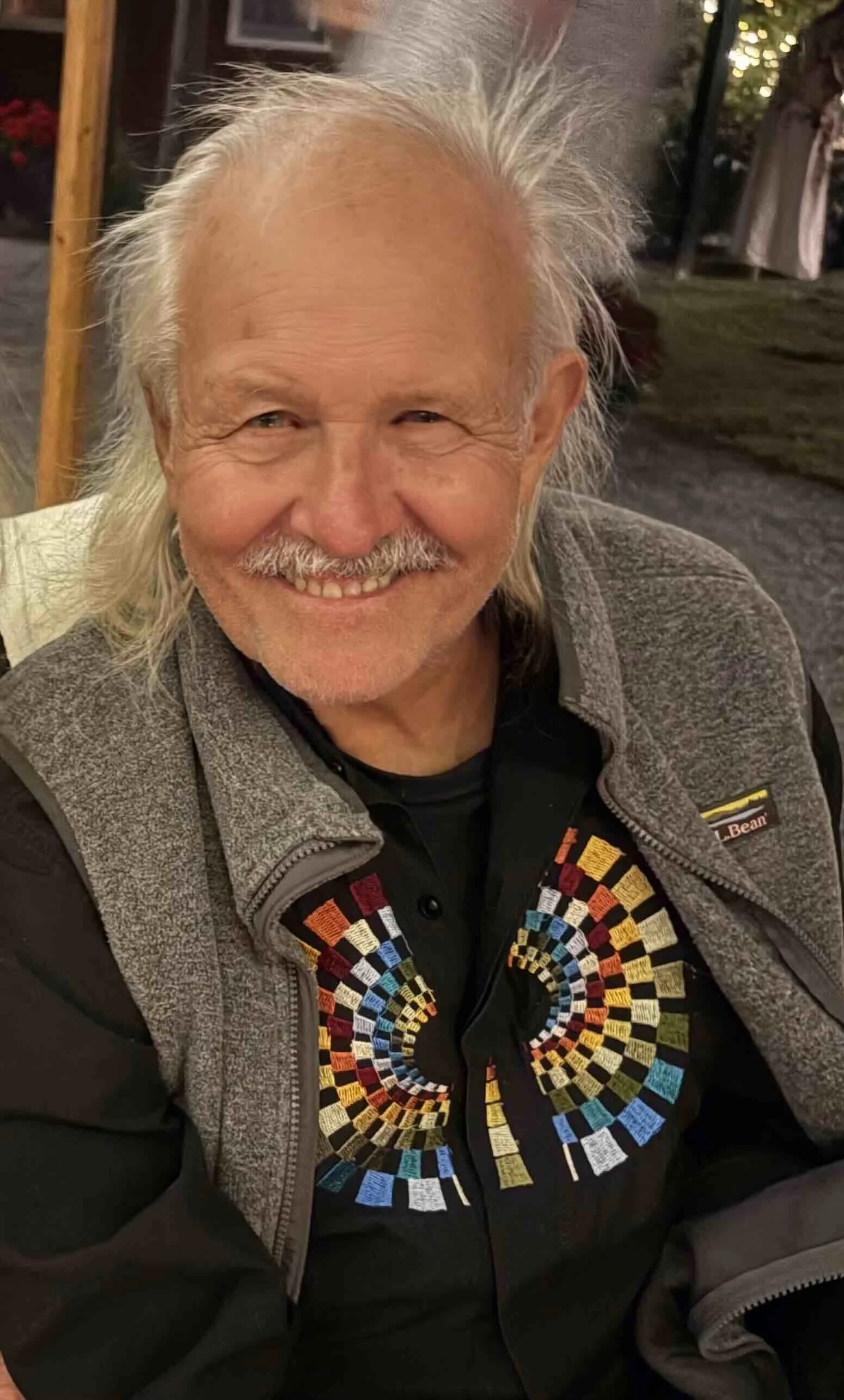 Man facing camera sitting in chair in a grey vest.