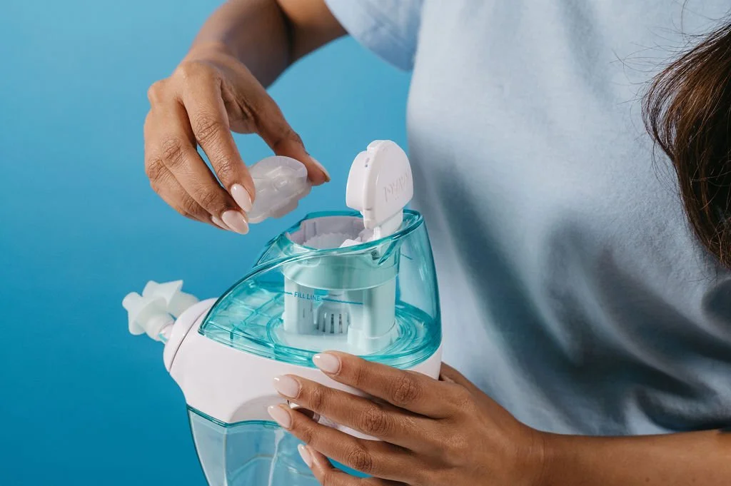 A person filling a humidifier with water from a small bottle against a blue background.