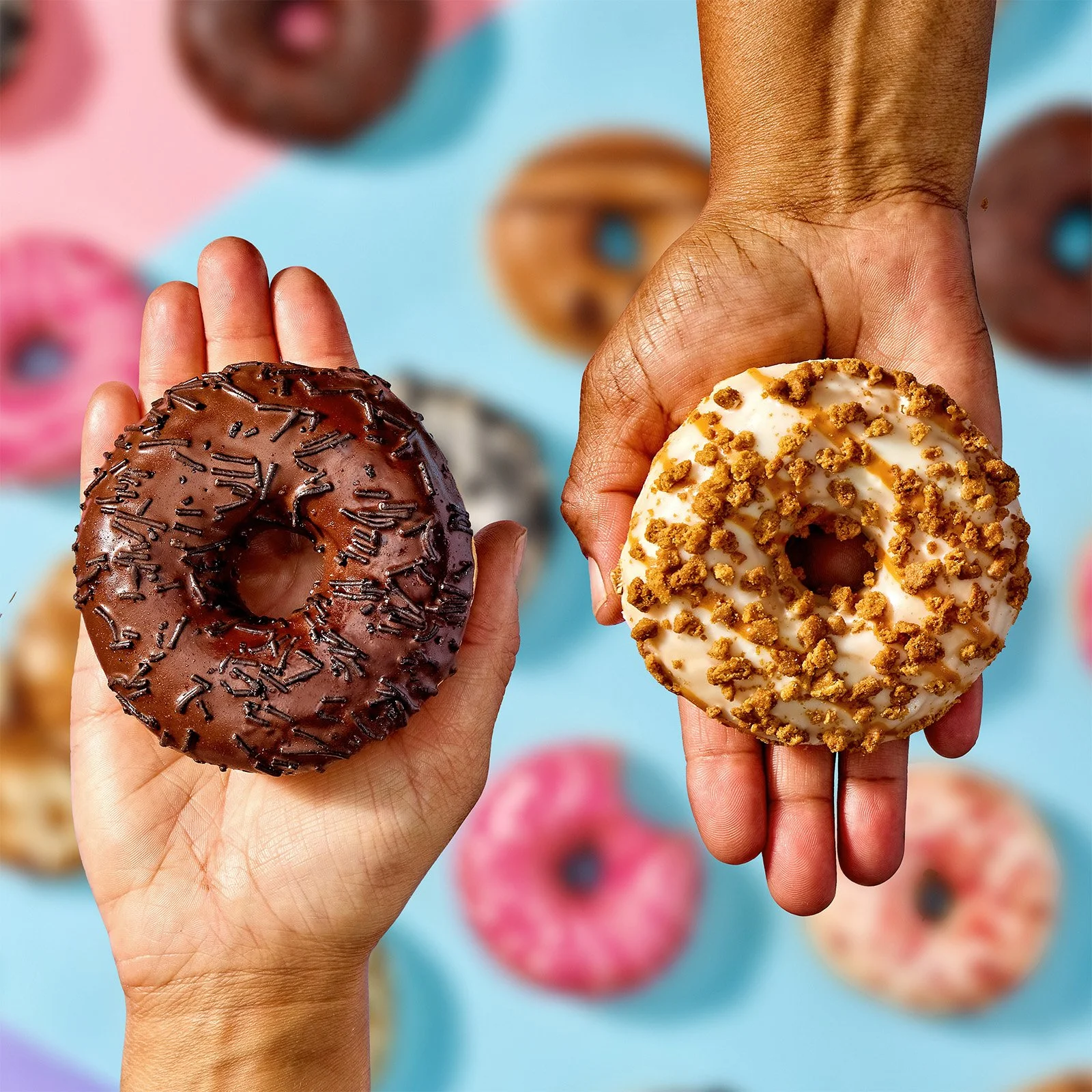 Two people holding donuts with different toppings, surrounded by more colorful donuts on a blue background.
