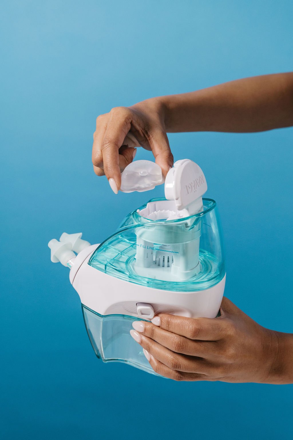 A person filling a small portable nebulizer with a clear nebulizer mask against a blue background.
