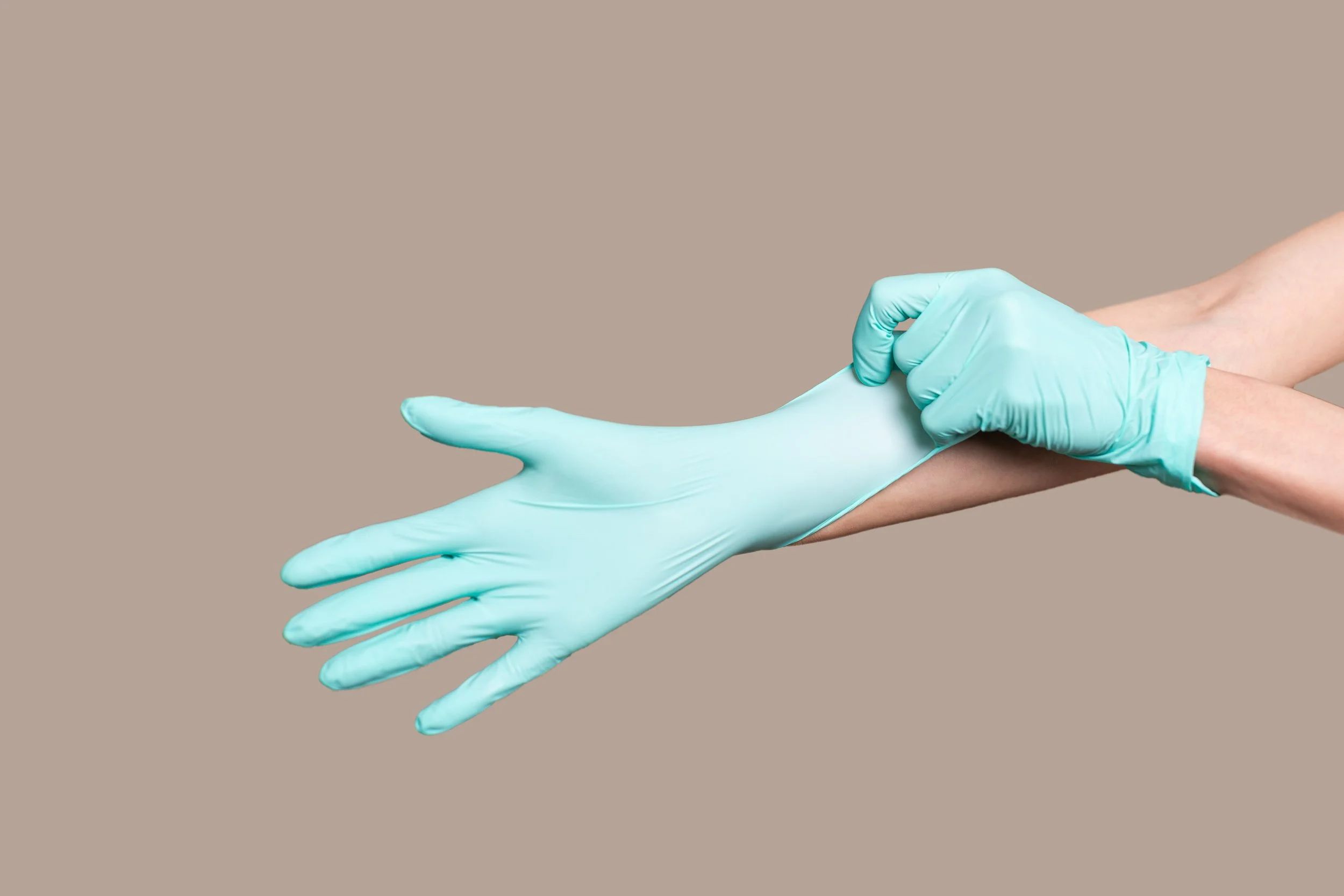 A healthcare professional wearing light blue gloves adjusting the cuff of a patient's arm against a beige background.