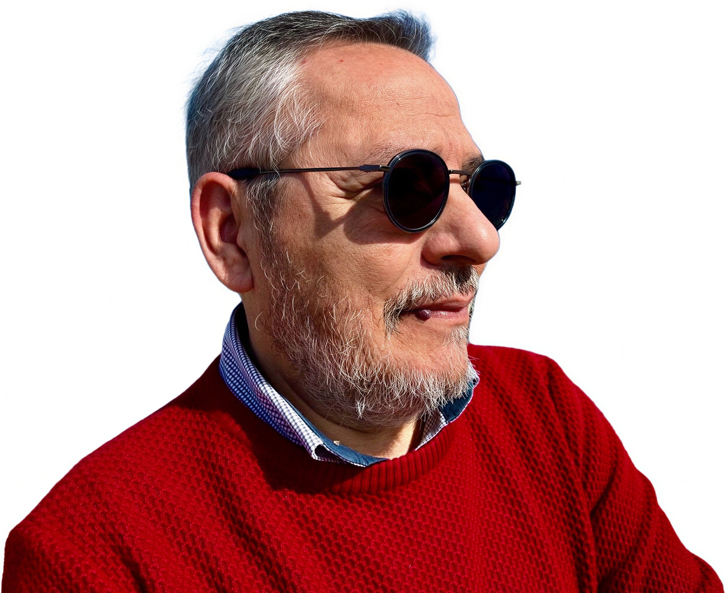 Uomo anziano con capelli grigi e barba, indossa occhiali da sole scuri, maglione rosso e camicia a quadri, sfondo bianco.