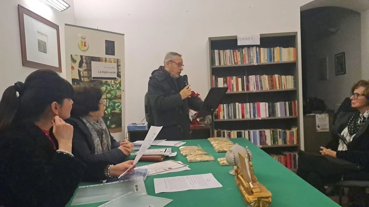 Un uomo sta facendo una presentazione a un gruppo di donne sedute intorno a un tavolo in una stanza con librerie e una cartellonistica.