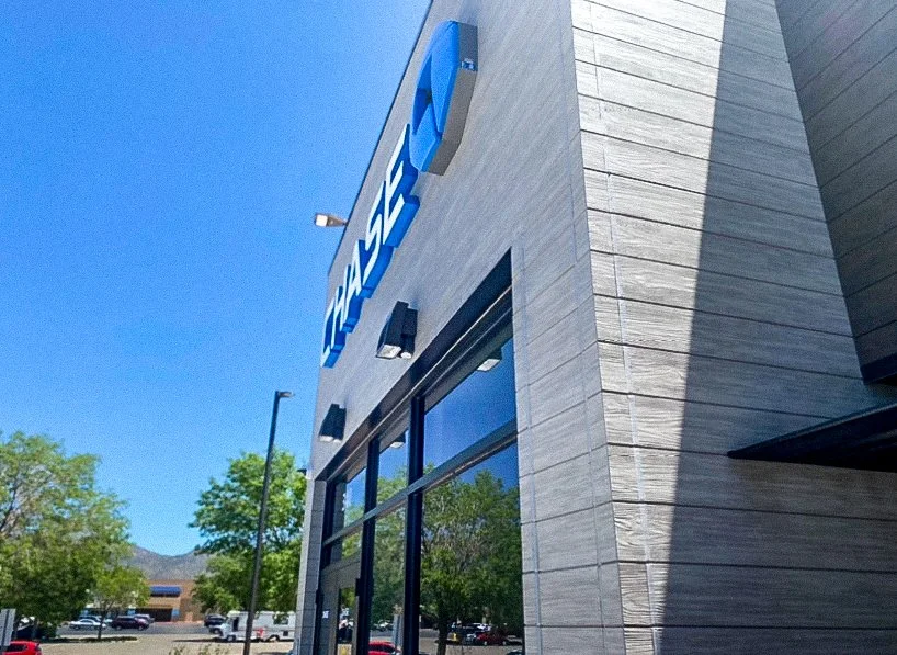 The exterior of a Best Buy electronics store with a large blue sign and glass windows on a sunny day.