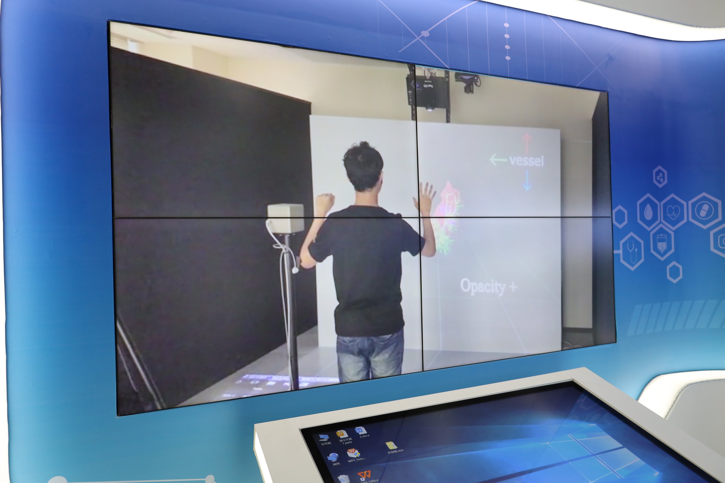 A person standing in front of a digital interactive screen that shows a colorful diagram with arrows labeled 'vessel' and 'opacity+'.