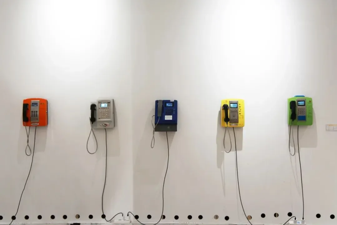 Five colorful payphones mounted on a white wall.