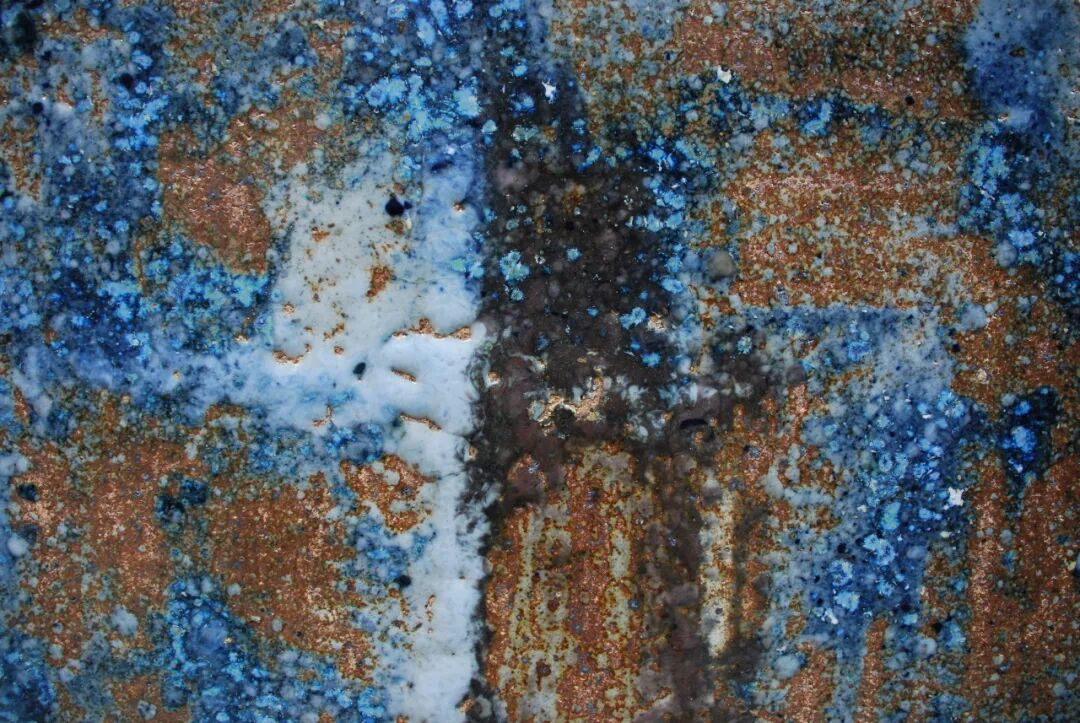 Close-up of a rusted and corroded metal surface with blue, white, black, and brown spots and textures.