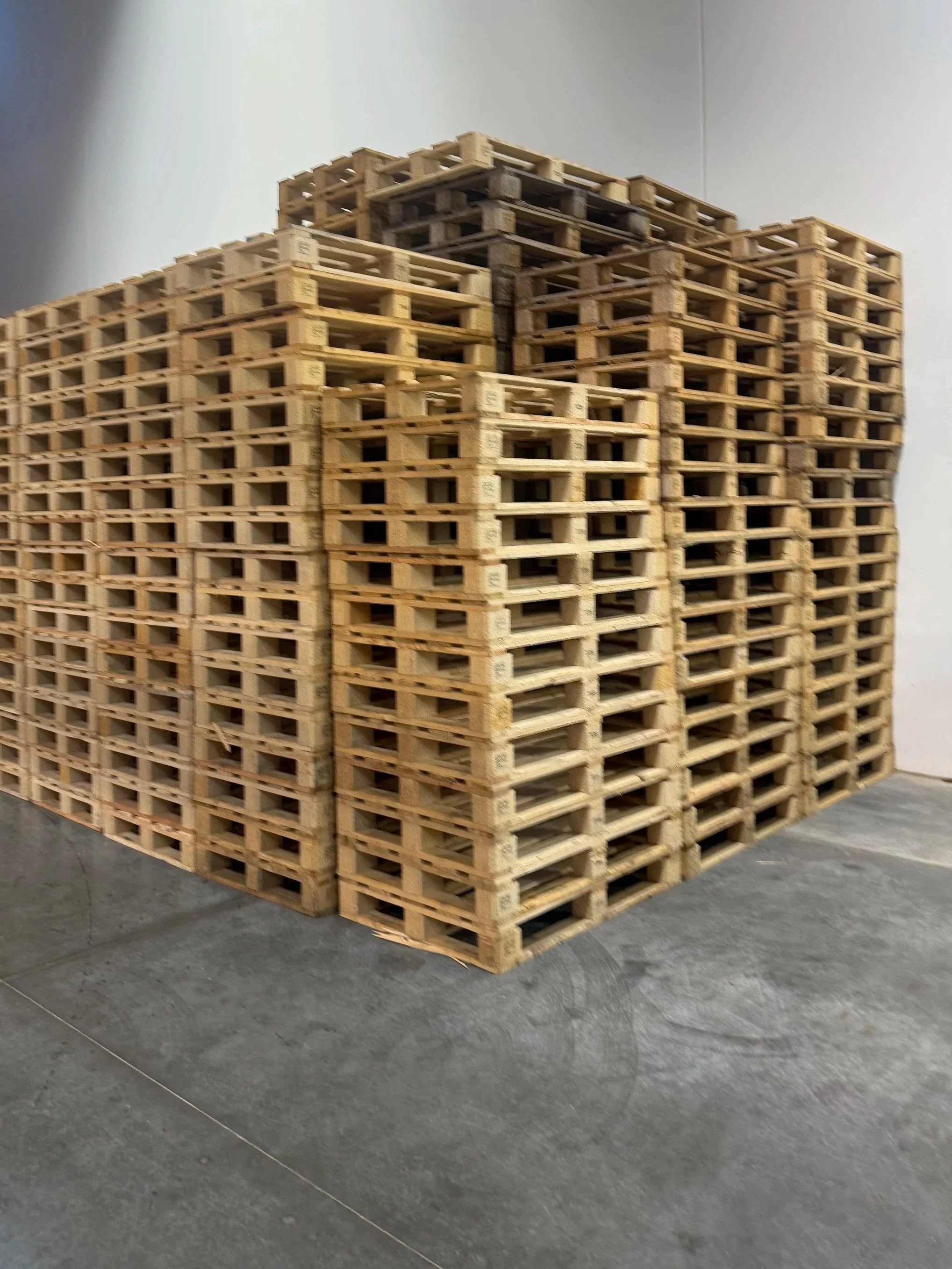 A large stack of empty wooden pallets arranged in a warehouse on a concrete floor.