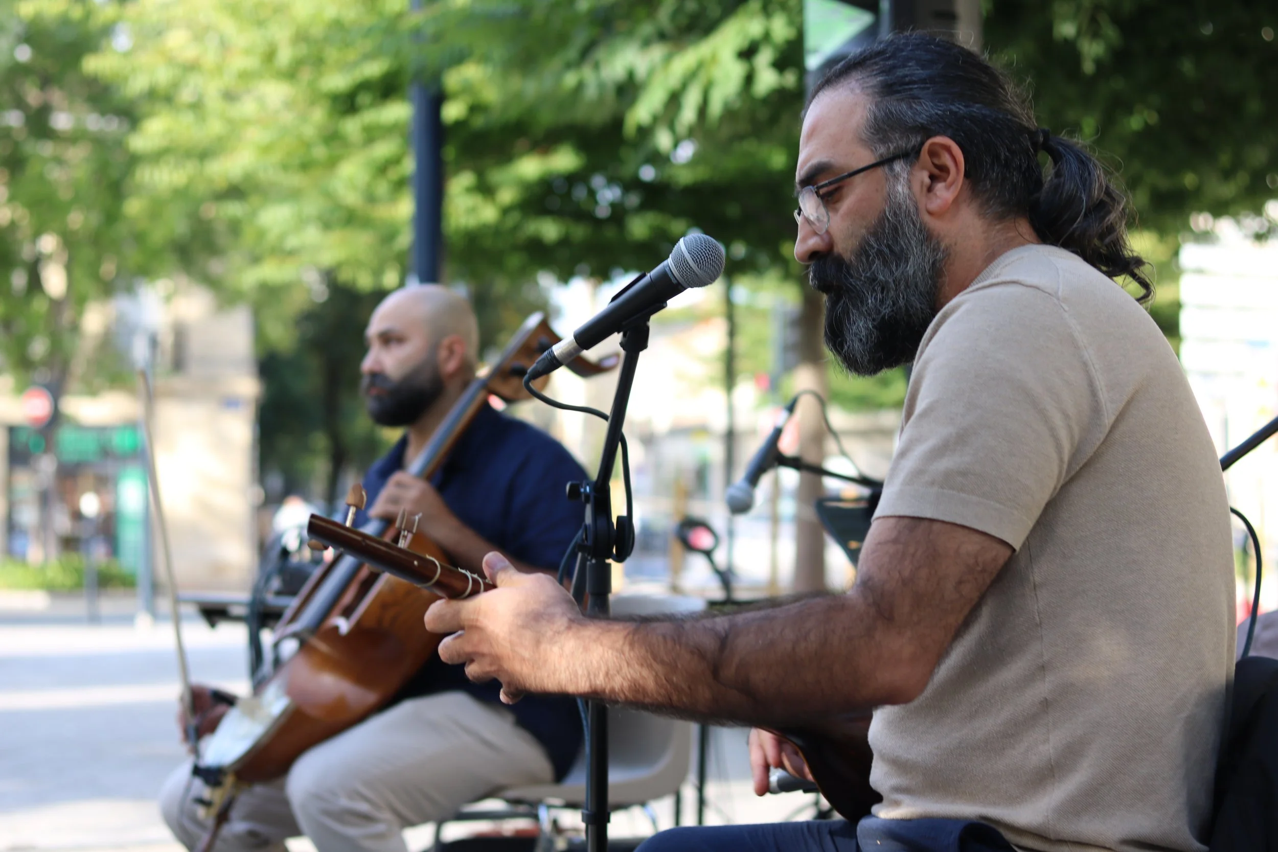 Deux musiciens jouent de la musique en plein air, un au geychak et l’autre au sitar, avec des arbres en arrière-plan.