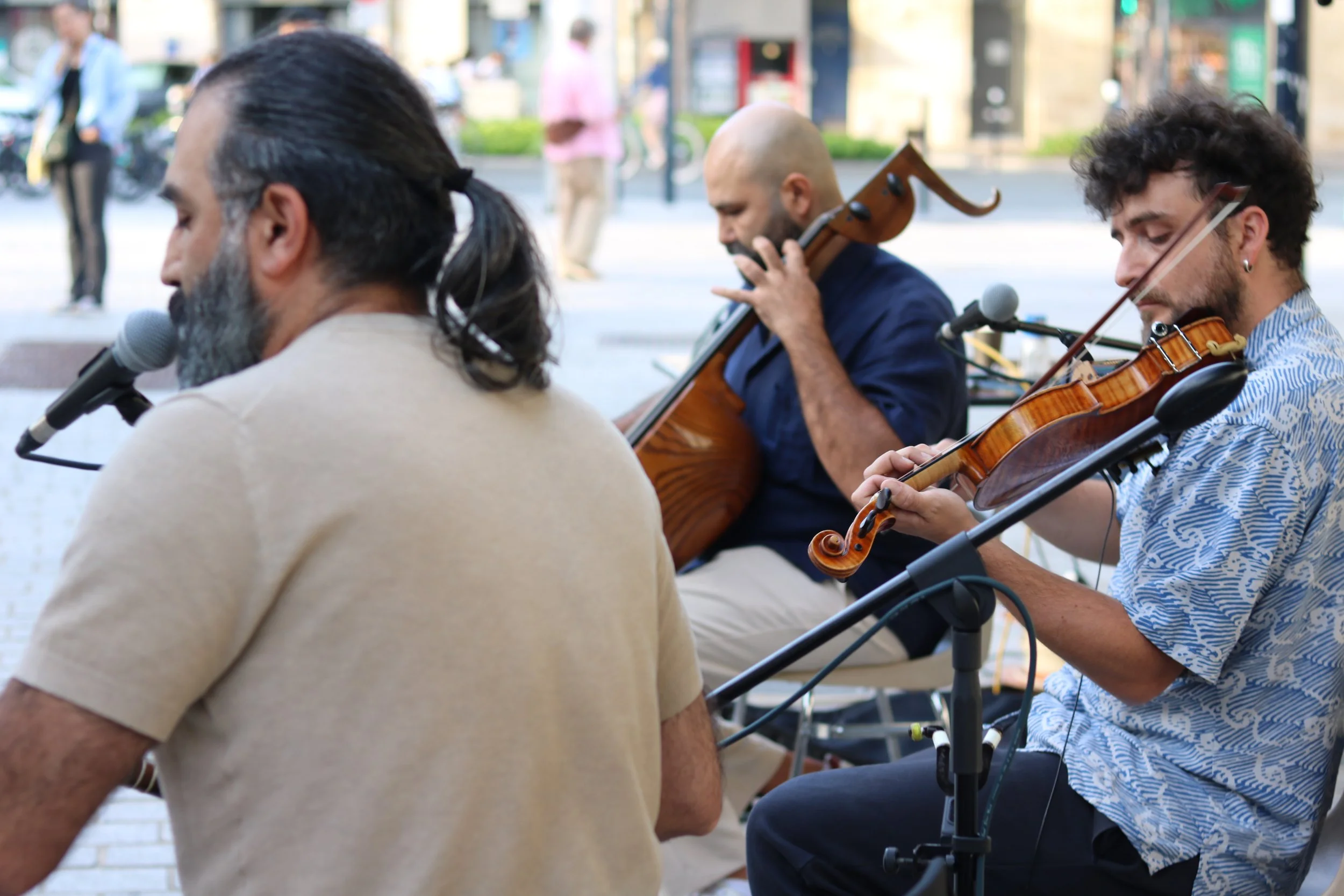 Trois musiciens jouent de leurs instruments lors d'une performance en plein air, avec un fond de rue.