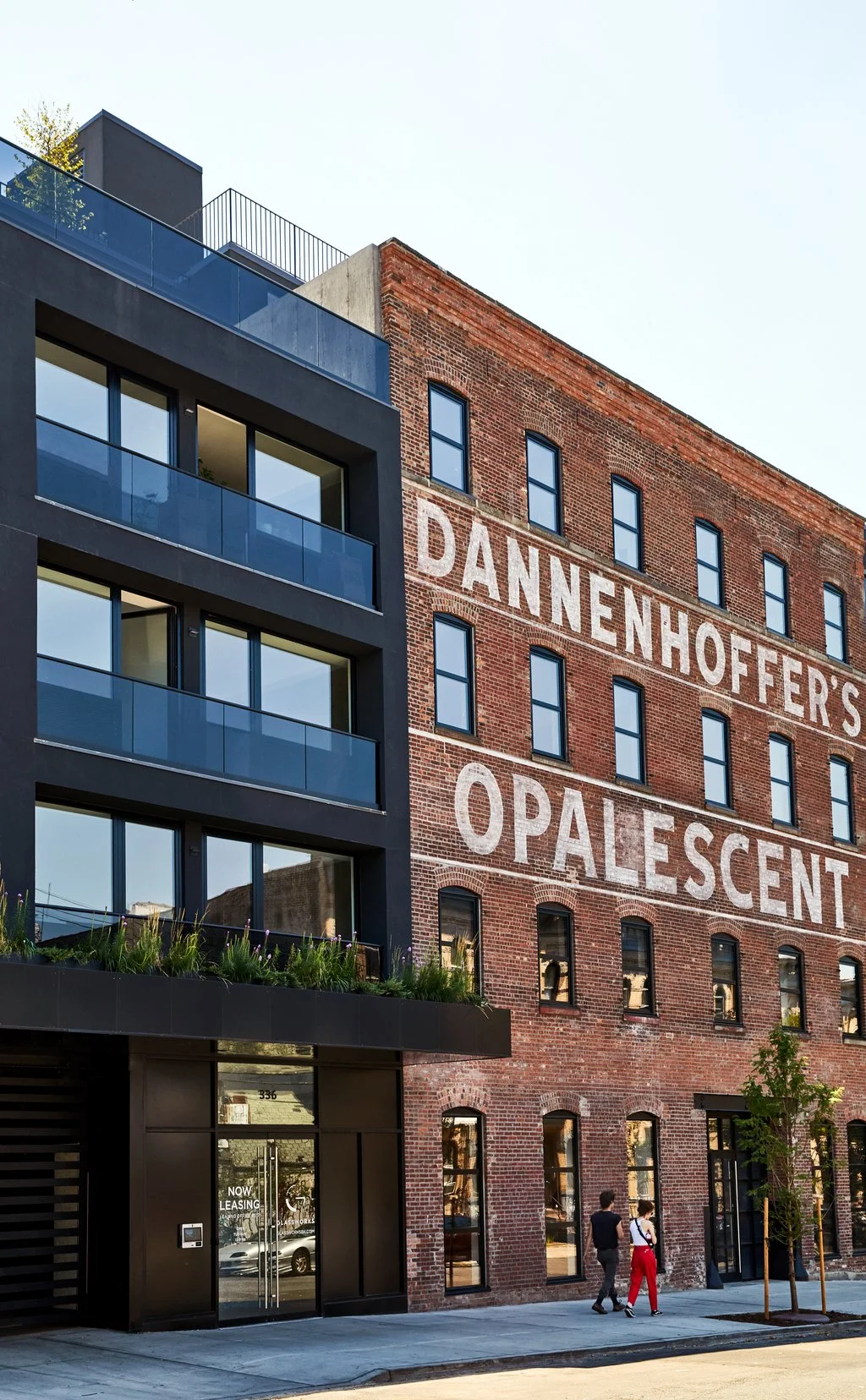 A modern building with large glass windows and balconies next to an old brick building with a mural reading 'Dannenhoffer's Opalescent'.