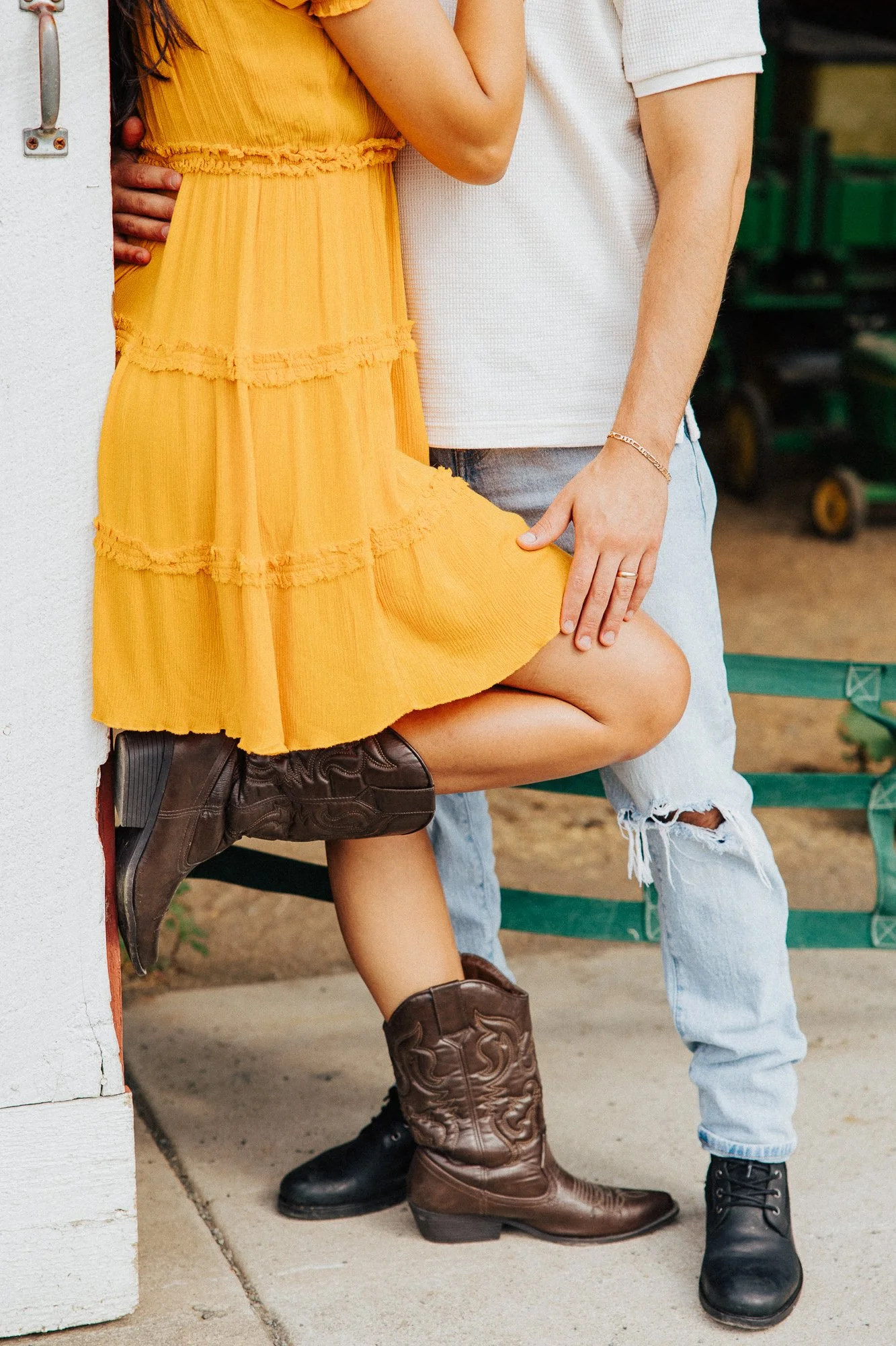 Close-up of a person in a white shirt and ripped jeans standing next to another person in a yellow dress and cowboy boots, with their hand resting on the person's thigh.