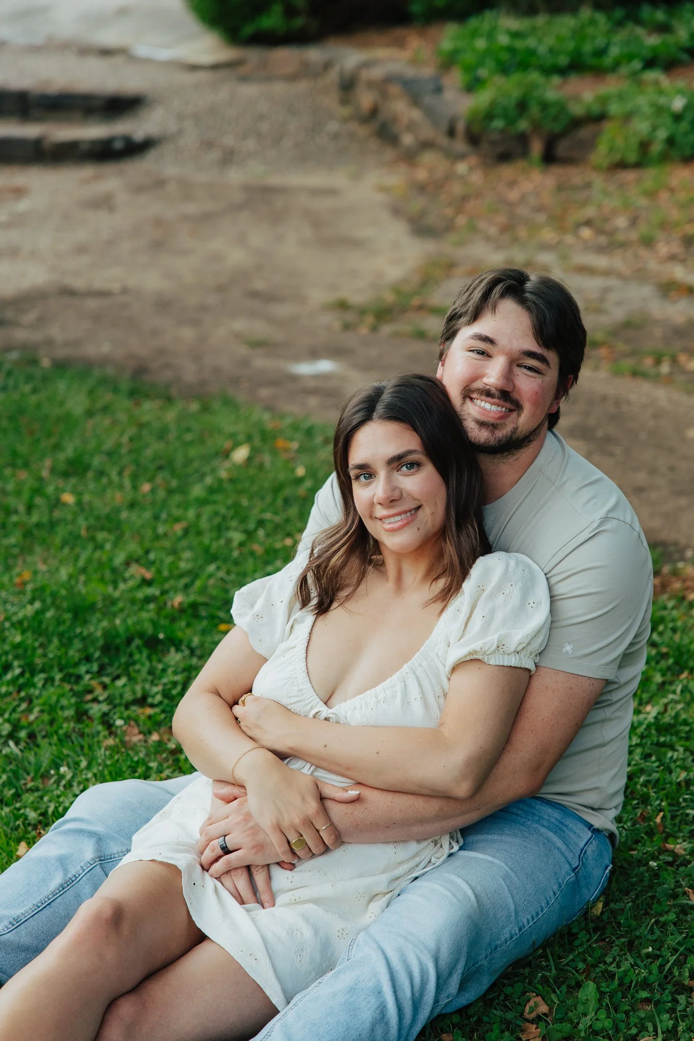 A young couple sitting on the grass outdoors, smiling and embracing each other.