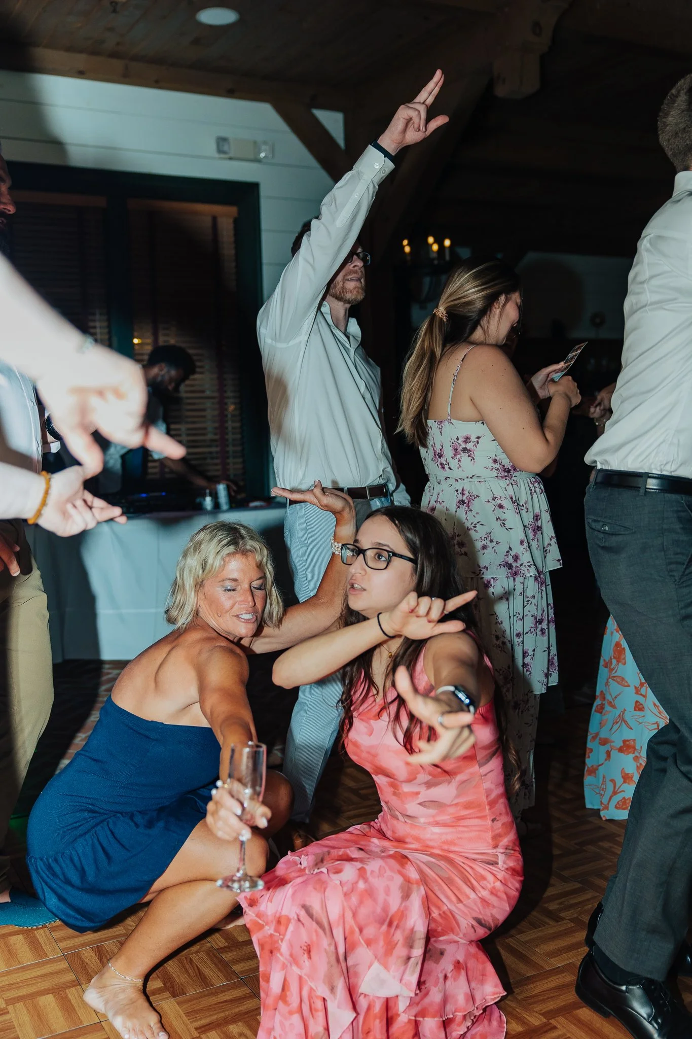 People dancing and celebrating at a party, with one woman in a pink floral dress sitting on the floor and others standing around.