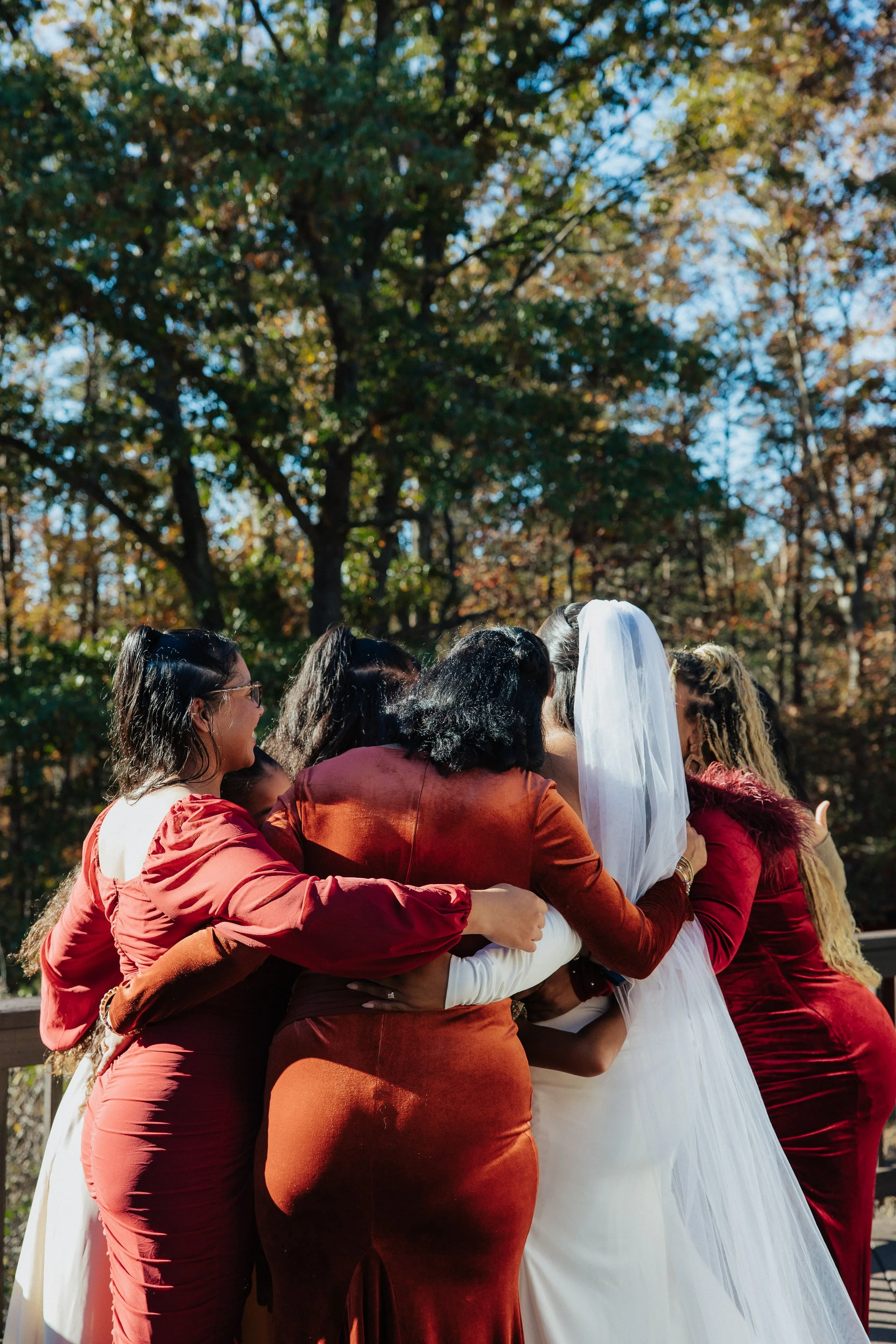 Group of diverse women embracing outdoors during a celebration, with trees and blue sky in the background.
