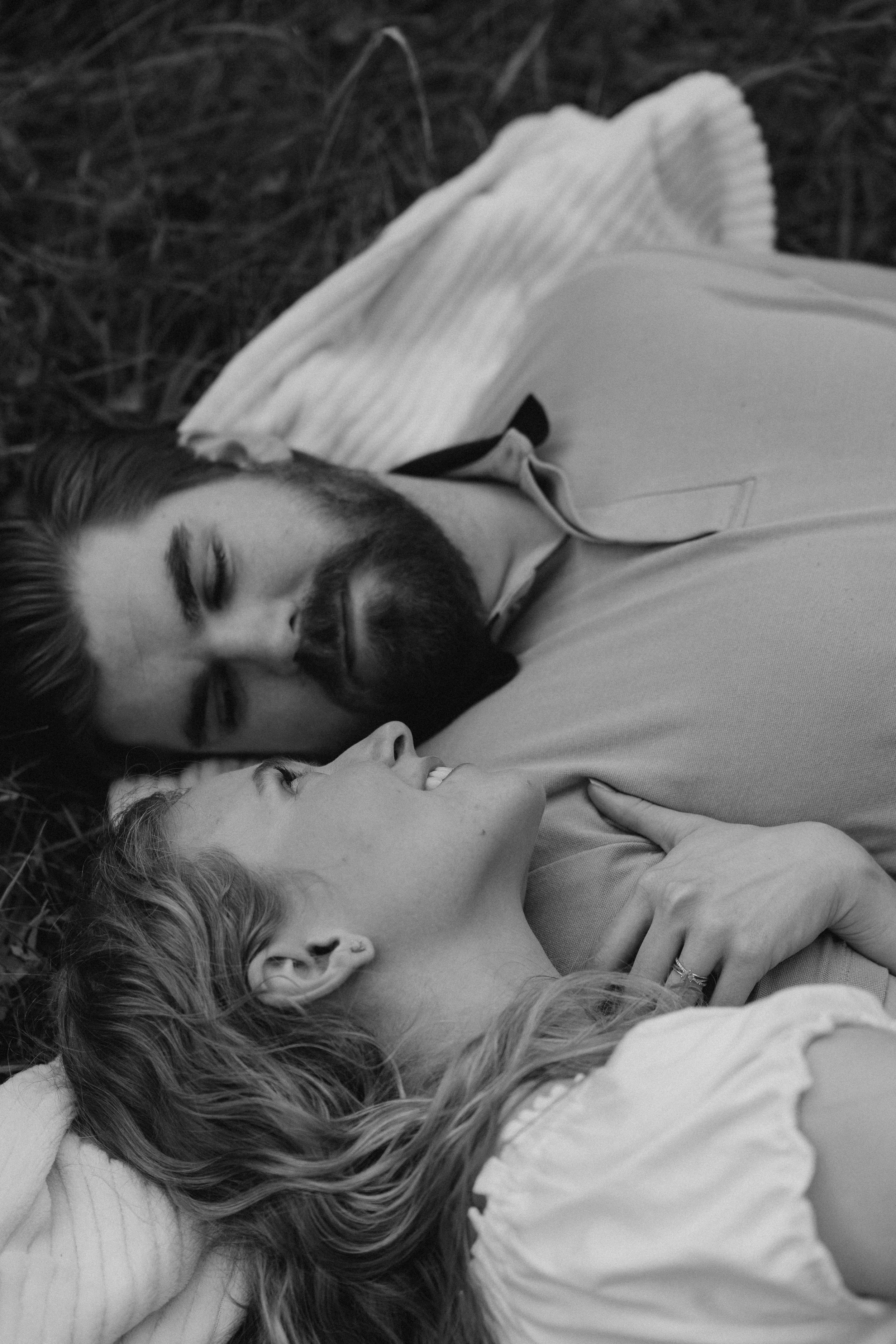 A black and white photo of a man and woman lying closely on the ground outdoors, gazing into each other's eyes.