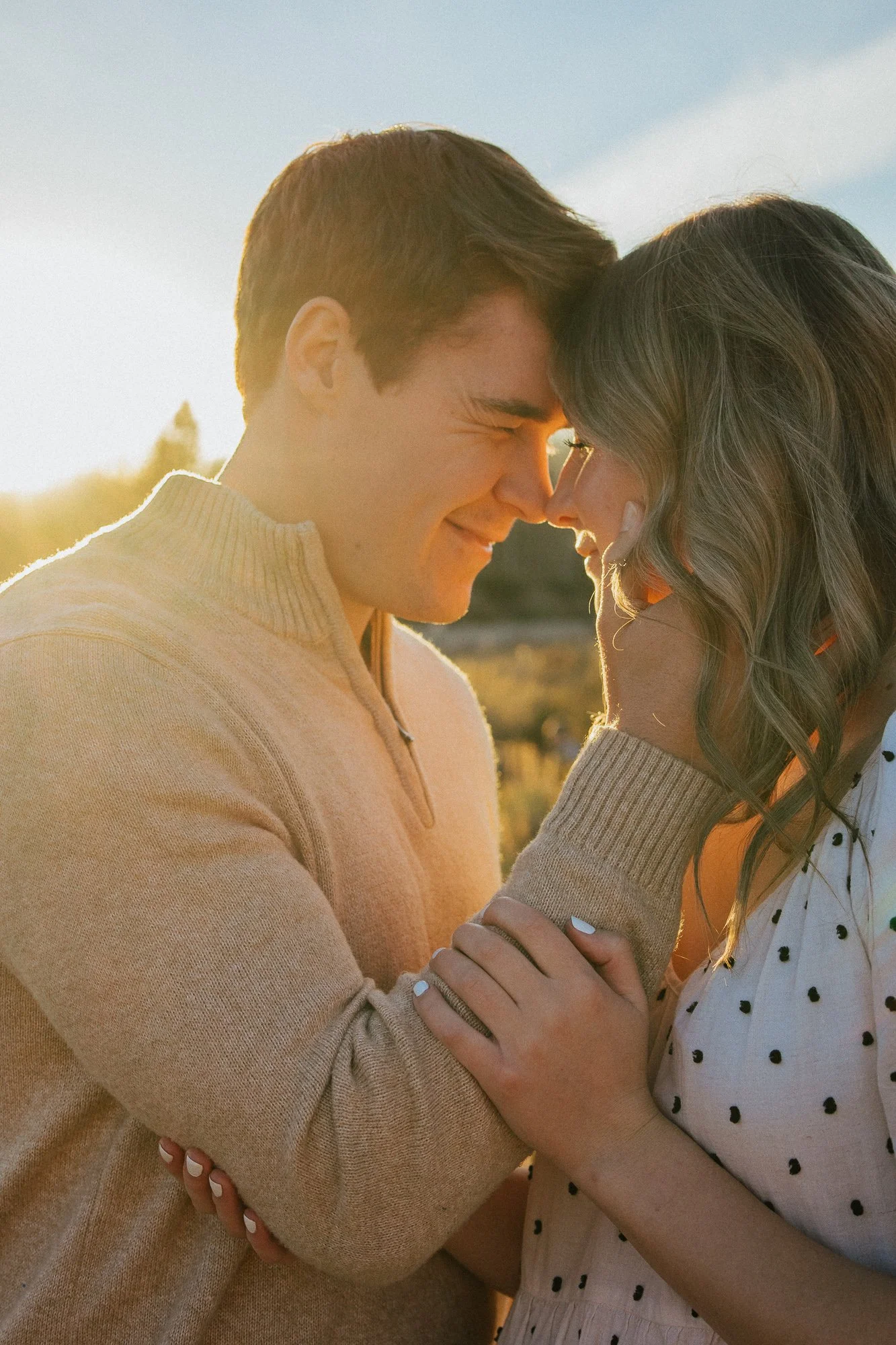 Two people, a man and a woman, gently touching their foreheads together and smiling in a sunset outdoor setting.