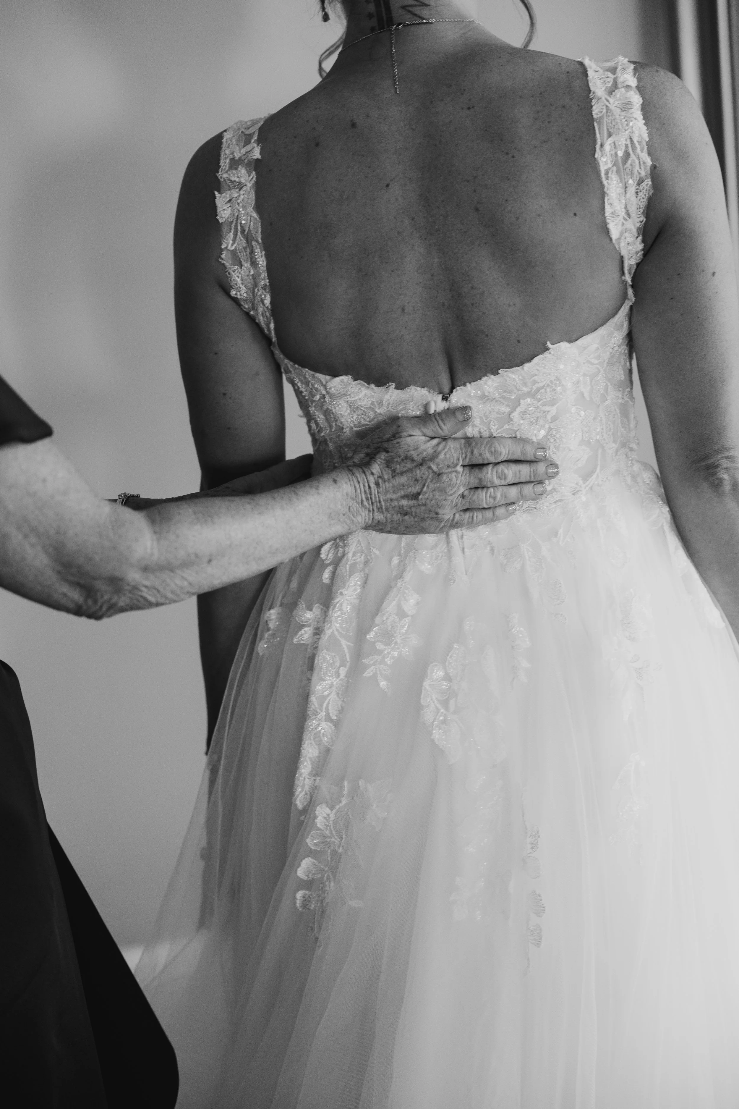 A woman wearing a wedding dress with lace shoulder details, holding her waist, and showing her back with a button closure.