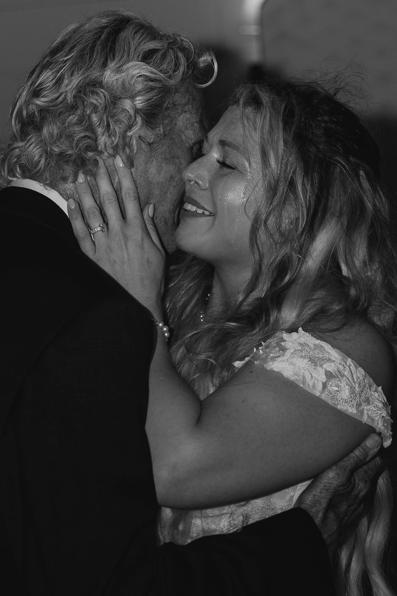 A black-and-white close-up photo of an elderly man and a middle-aged woman kissing each other on the lips with their eyes closed, holding each other closely.