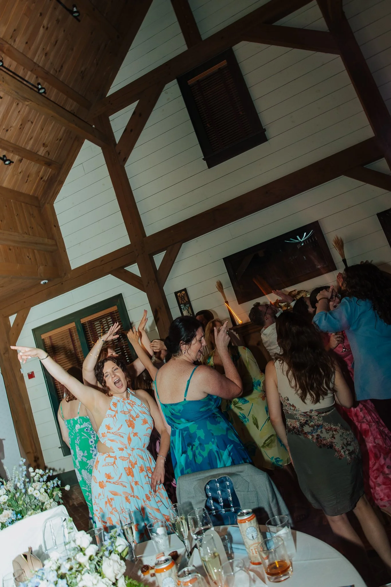 Group of people at a celebration, dancing and enjoying themselves indoors with a rustic wooden ceiling.