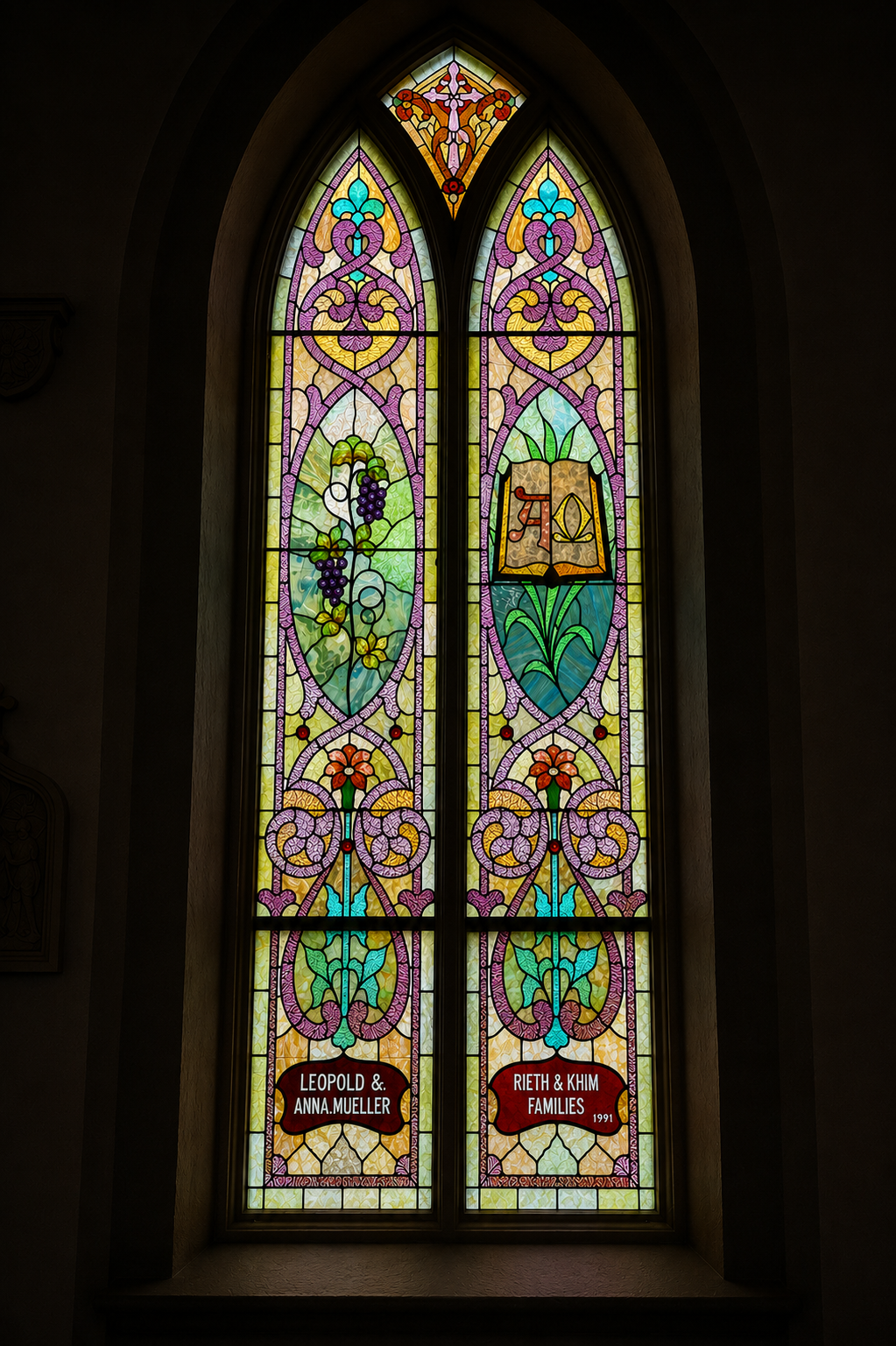 Colorful stained glass window with floral and geometric patterns, including grapes and flowers, and an open book with Hebrew writing. A red sign at the bottom reads "Leopold & Anna Mueller" and "Rieth & Khim Families 1991."
