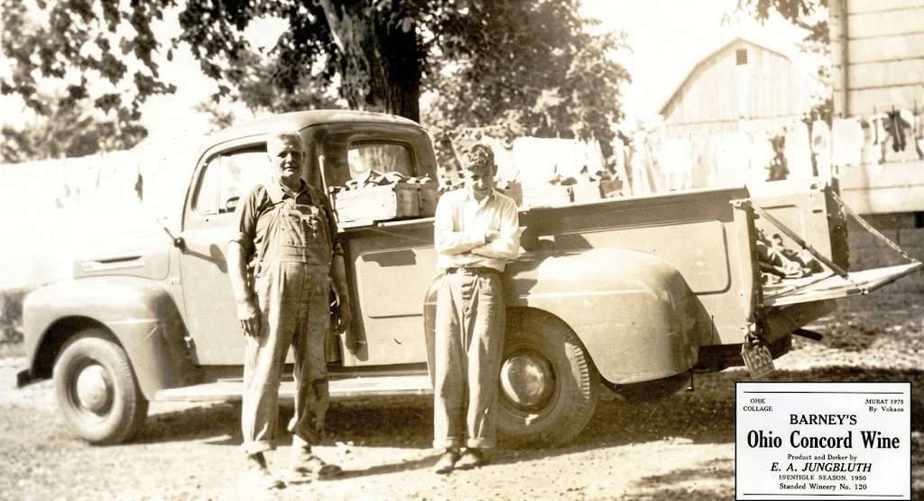 Two men standing next to a vintage pickup truck outdoors, with a barn and laundry hanging on a line in the background, and a label for Ohio Concord Wine from 1975 in the bottom right.