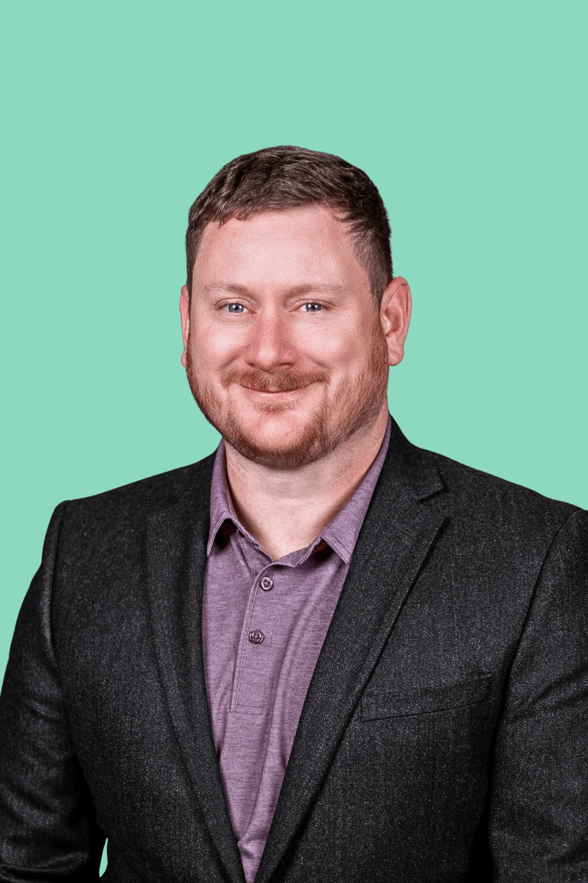 Bryce Bowen, founder of Full Ninety Marketing, wearing a dark gray blazer over a light purple dress shirt, smiling against a mint green background.