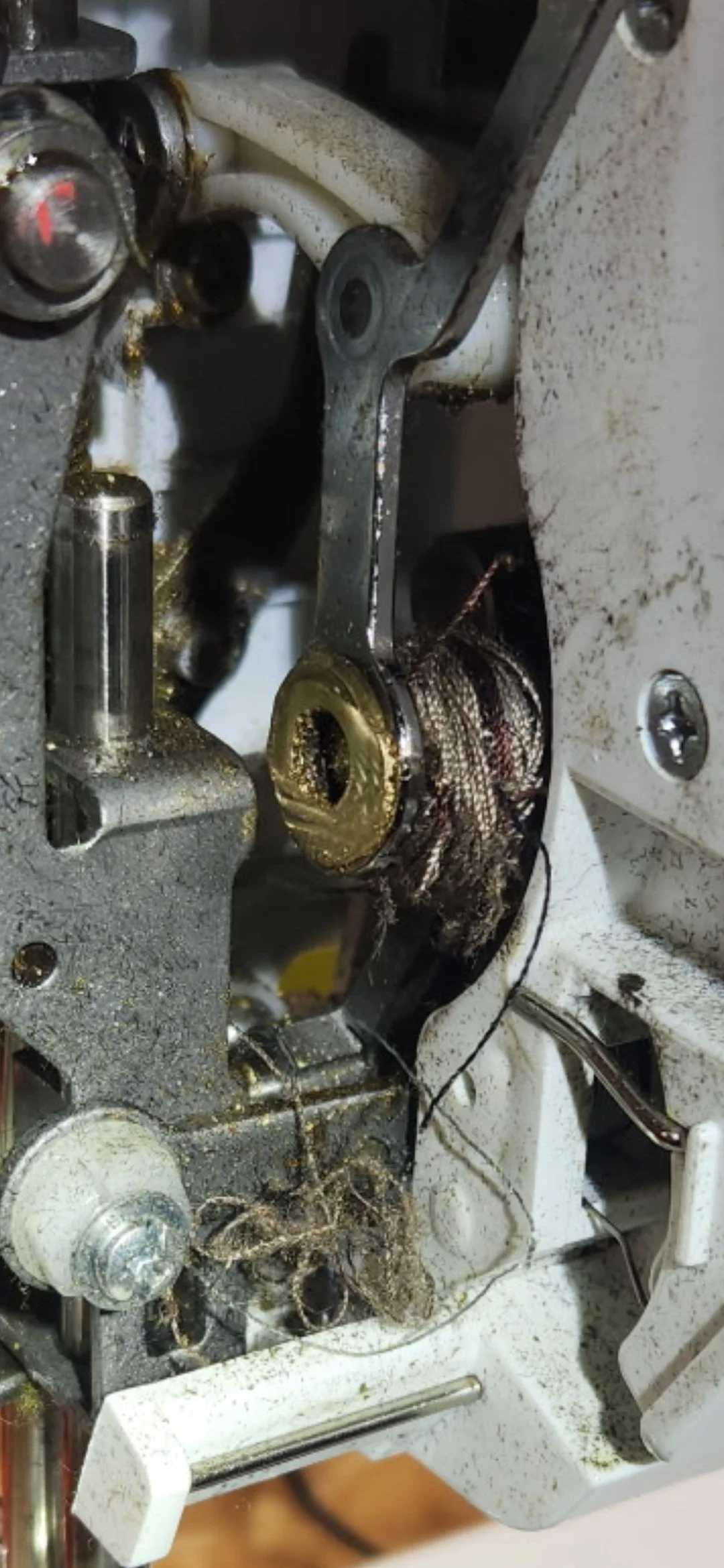Close-up of the internal components of a malfunctioning or dirty sewing machine, with visible dirt, lint, and tangled threads.