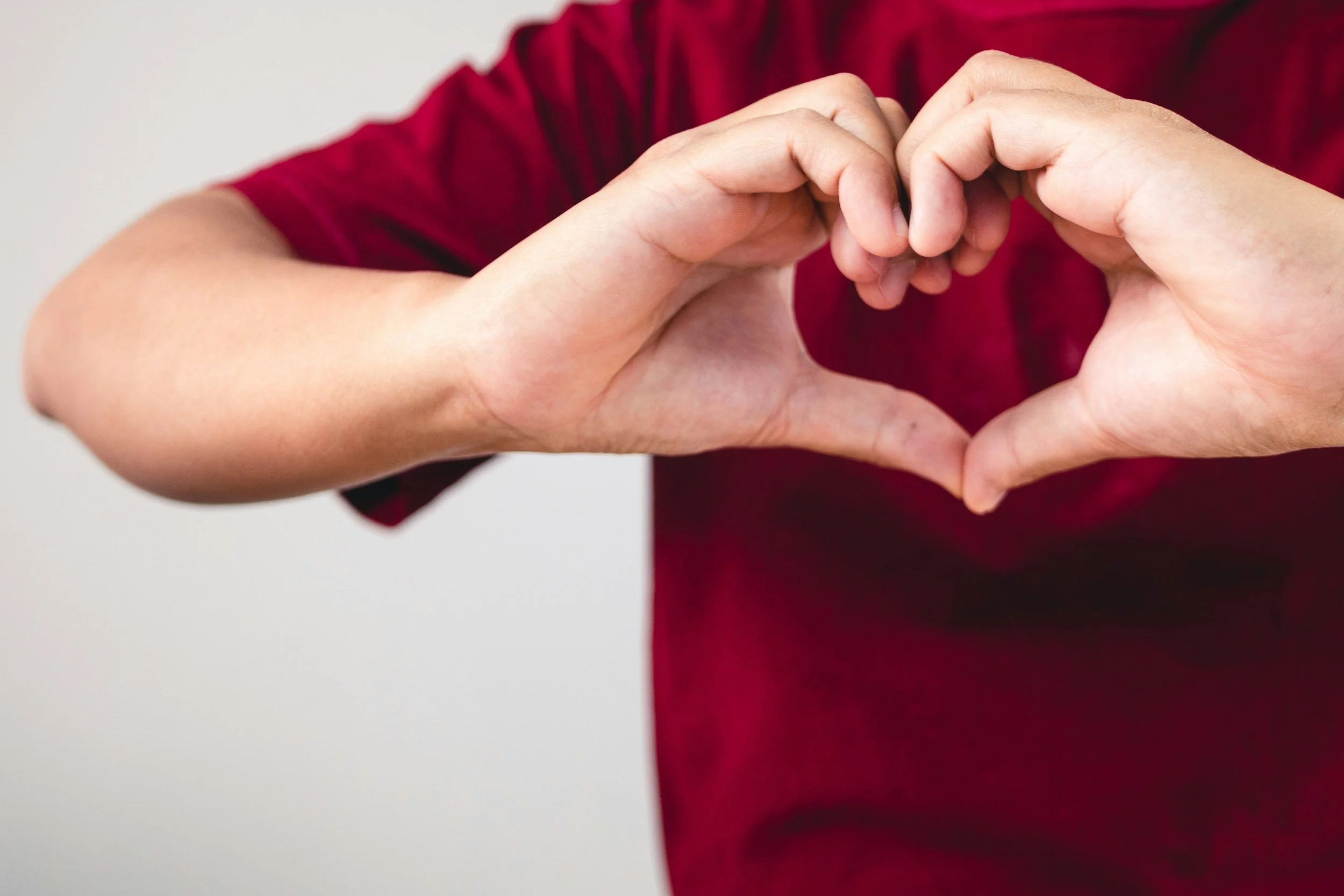 A person wearing a red shirt forms a heart shape with their hands.