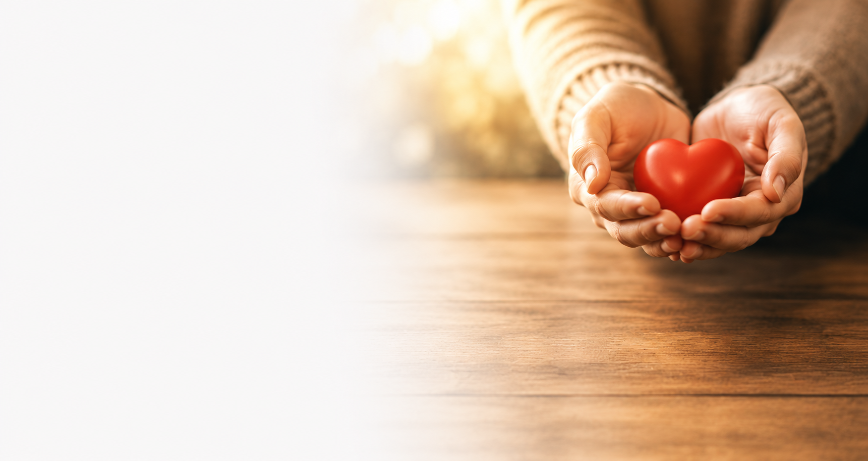 Person holding a red heart-shaped object in their hands over a wooden surface.