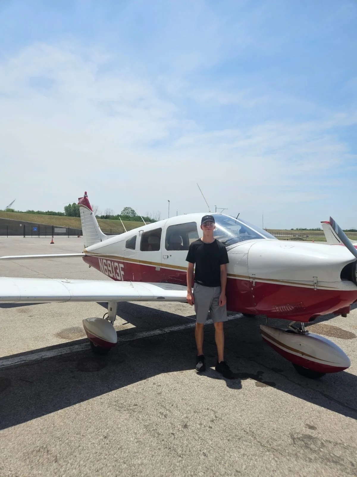 Pierce Jackson standing in front of a small white and red airplane on an airport tarmac on a sunny day.