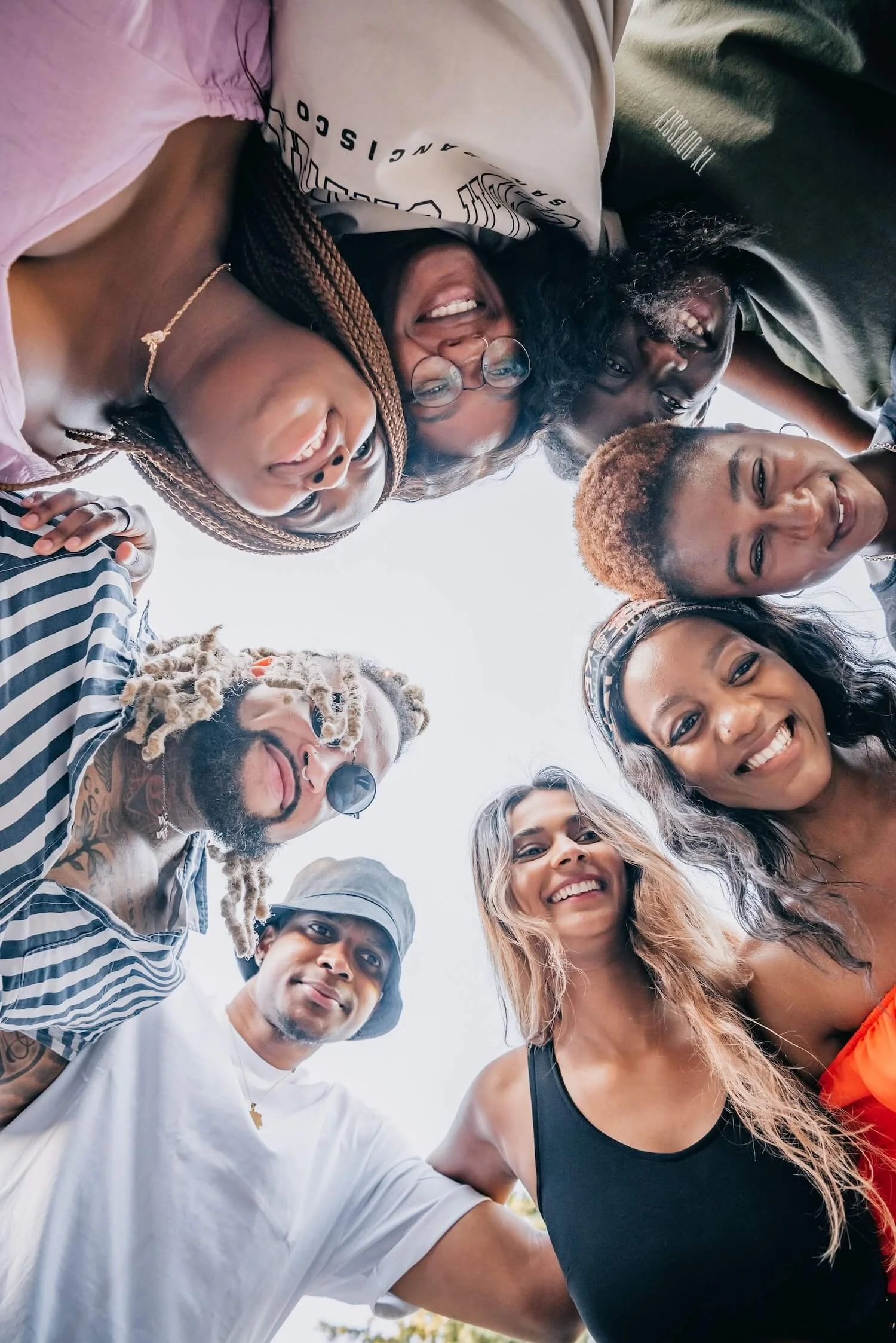 Group of friends laughing together in a huddle against a bright sky